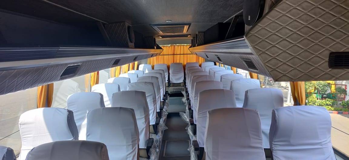 Interior of a bus featuring white-covered seats, bright curtains, and overhead storage compartments.