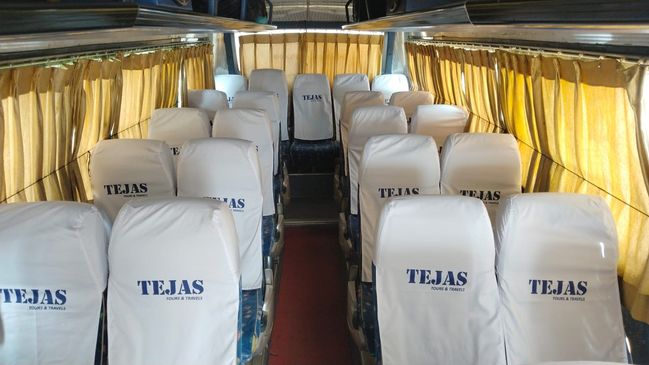Empty bus interior with white-covered seats and a green aisle, illuminated by natural light through large windows.
