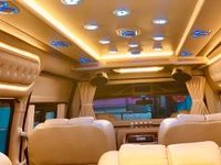 Luxurious van interior featuring plush seating, mood lighting, and a sleek design with sound system controls visible.