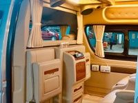 Luxurious van interior featuring beige leather seats, wooden accents, curtains, and a bright overhead light.