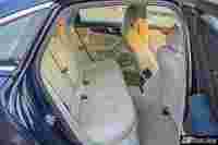 Spacious, light-colored leather backseat of a luxury car with seatbelts fastened.