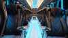 Empty bus interior featuring sleek black leather seats with plastic coverings and blue ambient lighting along the aisle.