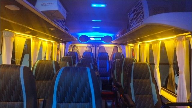 Interior of a bus with neatly arranged seats, illuminated by blue and yellow lights, curtains at the windows.