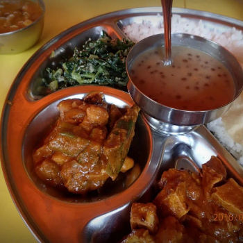 A Plate Of Rice With A Few Types Of Vegetarian Dishes, A Bowl Of Dahl, A Bowl Of Dessert And A Glass Of Cold Water
