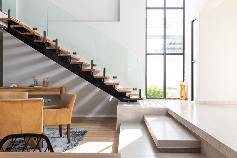 Two-point perspective of a modern staircase with soft daylight streaming through a large window.