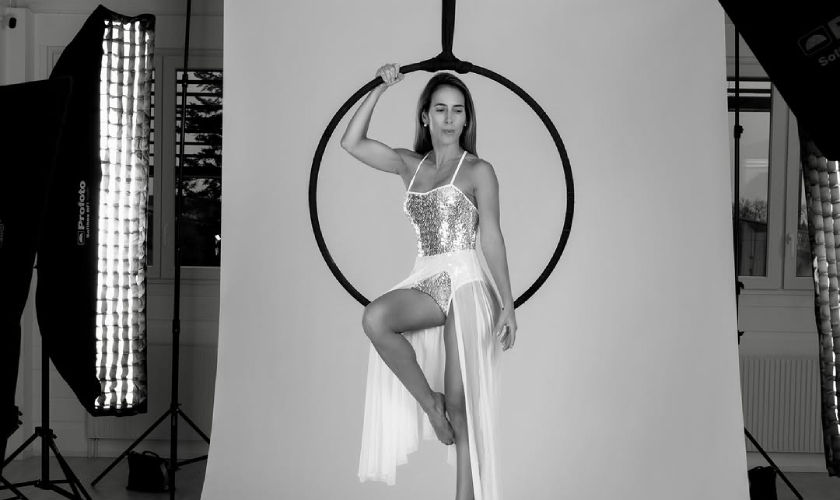 Group of people in a brightly lit studio practicing pole dance moves, smiling and wearing athletic attire, emphasizing fitness transformation.
