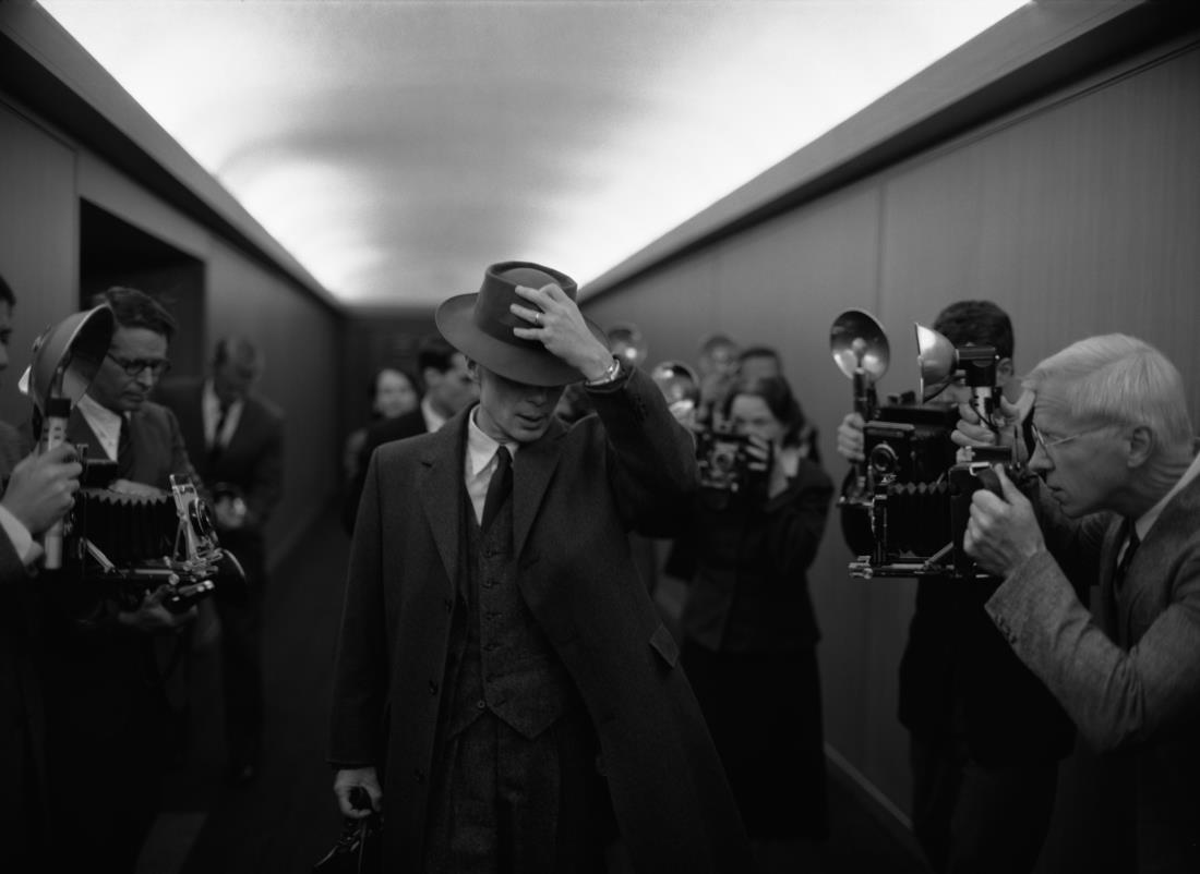a black and white photo of a man hiding his face with a hat surrounded by journalist