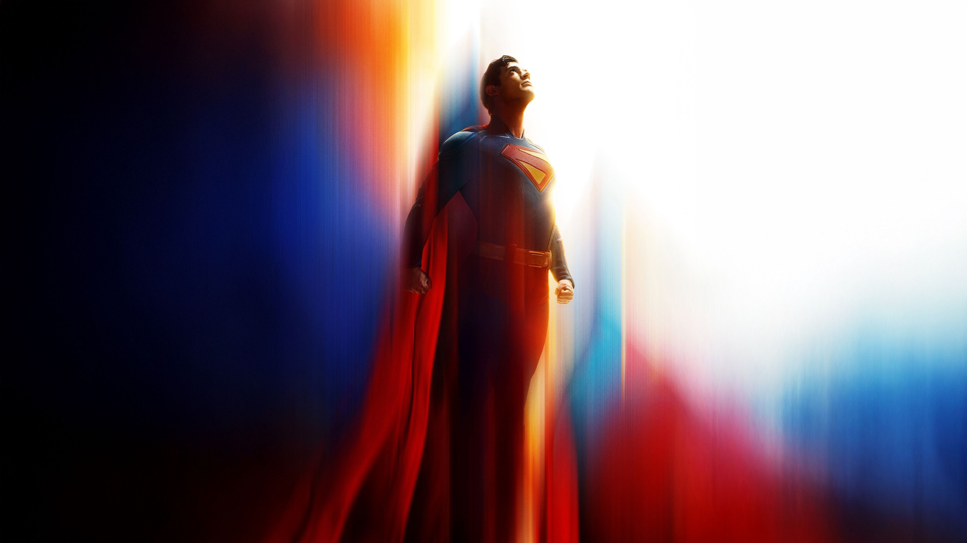 a full-body shot of a man in his suit and cape, looking upwards with a bright light behind him.