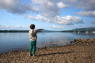 Captivating Lakeside Bliss - A young boy's wonderment brings the sky and water together as he points to the soaring kite, blending joy and tranquility amidst nature's serene backdrop.