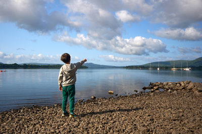 Captivating Lakeside Bliss - A young boy's wonderment brings the sky and water together as he points to the soaring kite, blending joy and tranquility amidst nature's seren
