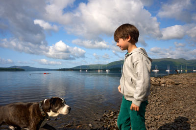 Serene lake shore bond between boy and dog; gray sweatshirt and soaring kite add a touch of style and adventure