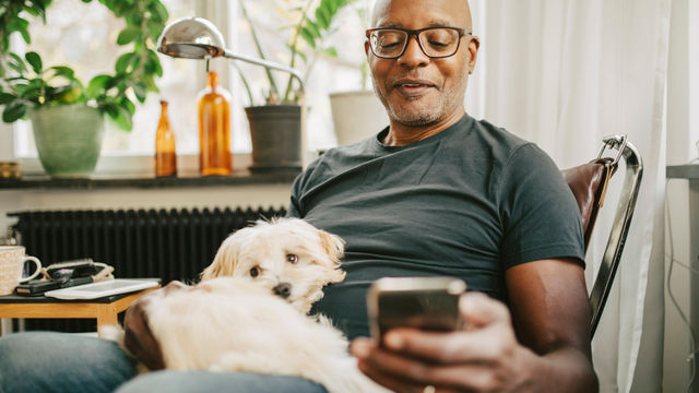 Ouderen man met hond op telefoon op de bank 1151007843