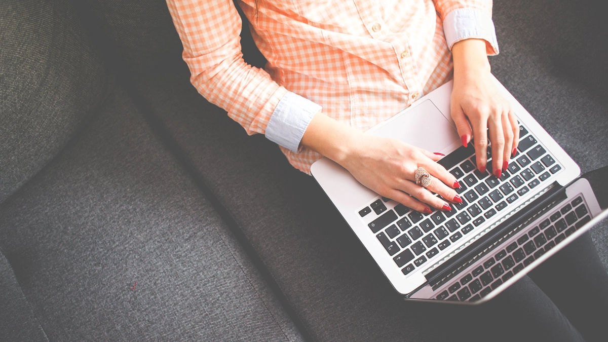 Mulher sentada no sofá, ecrevendo no blog em seu notebook