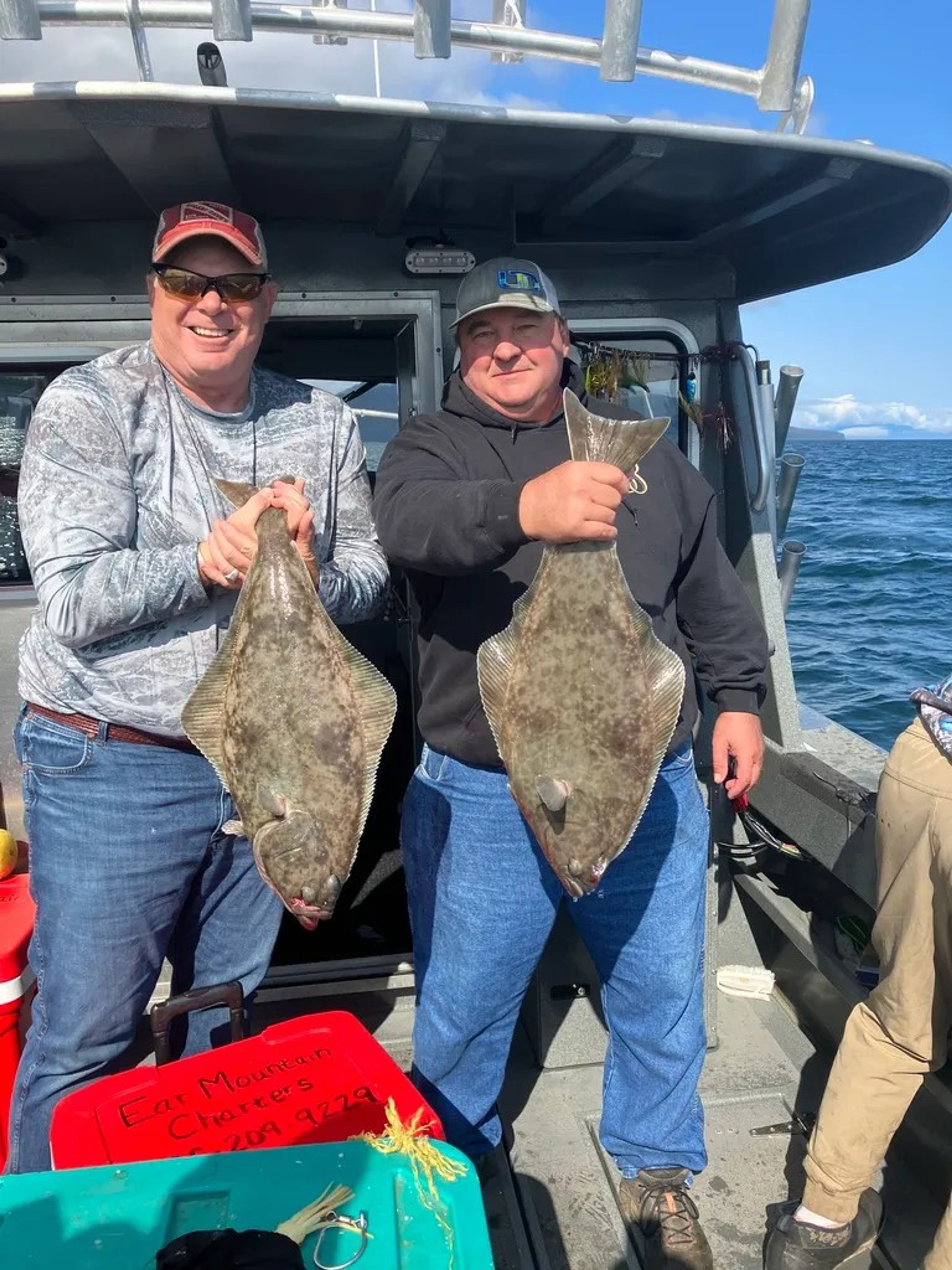 Two fishermen holding large flatfish on a boat in the ocean.