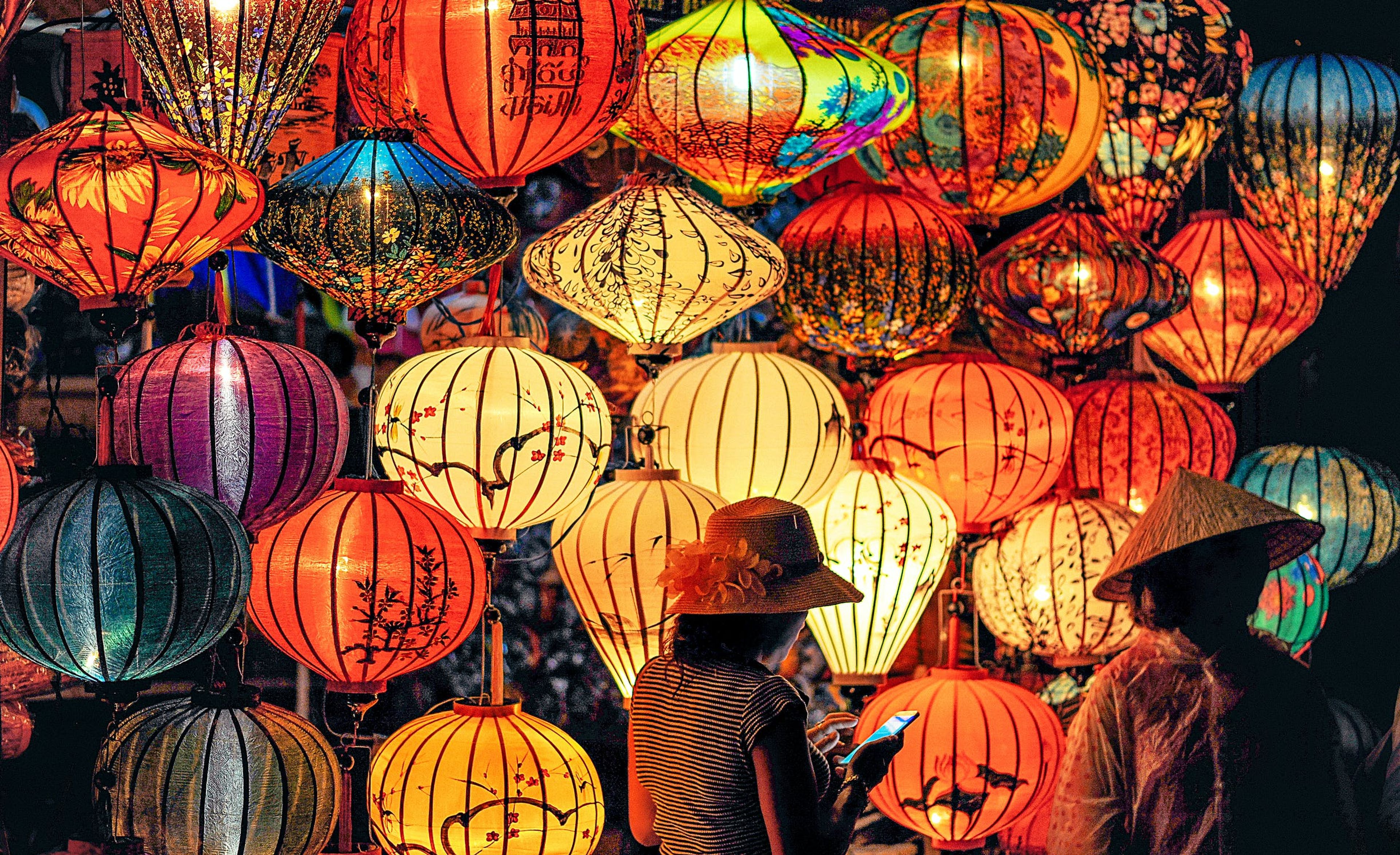 Colorful lanterns illuminate a night market with two people in traditional hats.