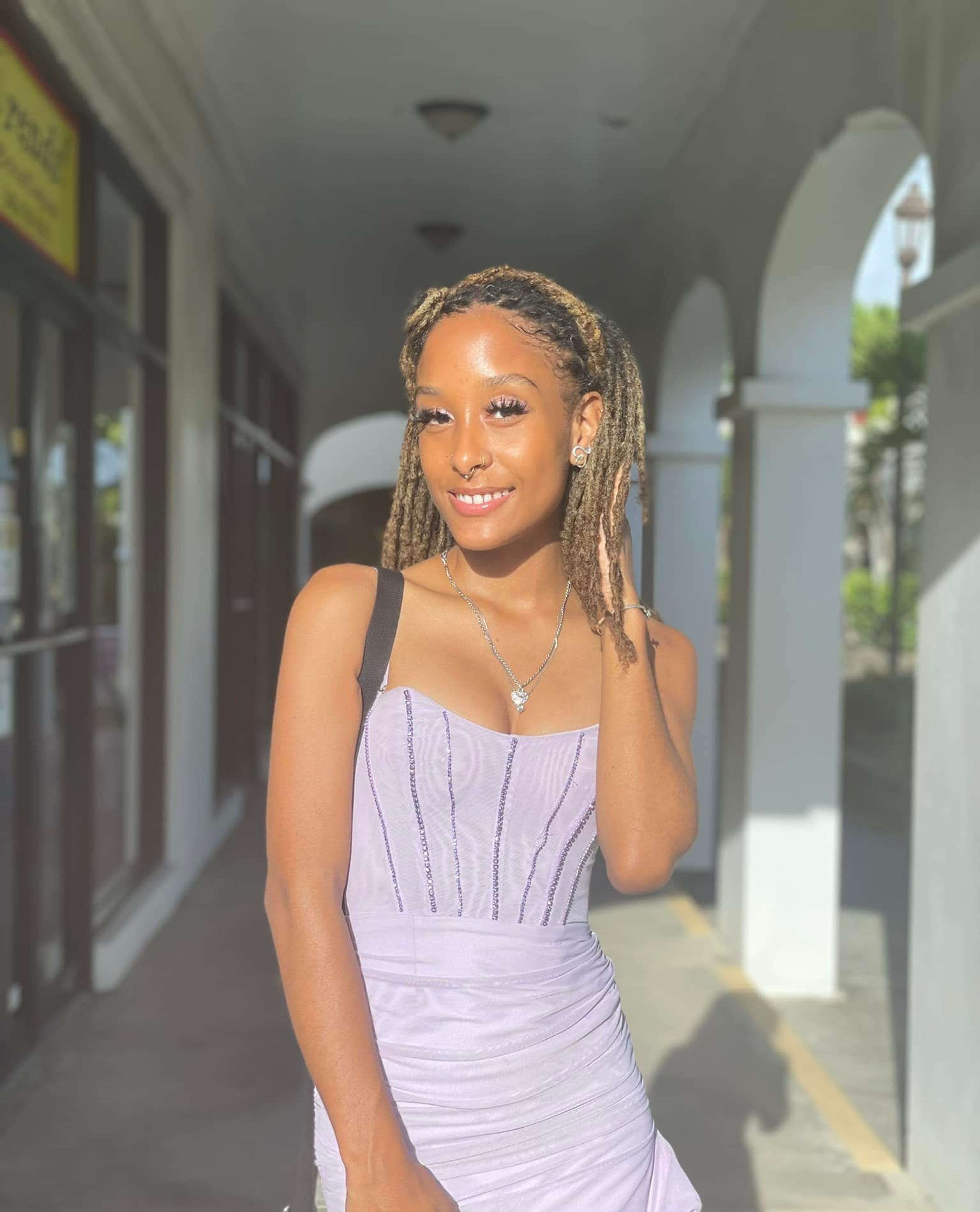 Person in a lavender dress posing in a corridor with arches.