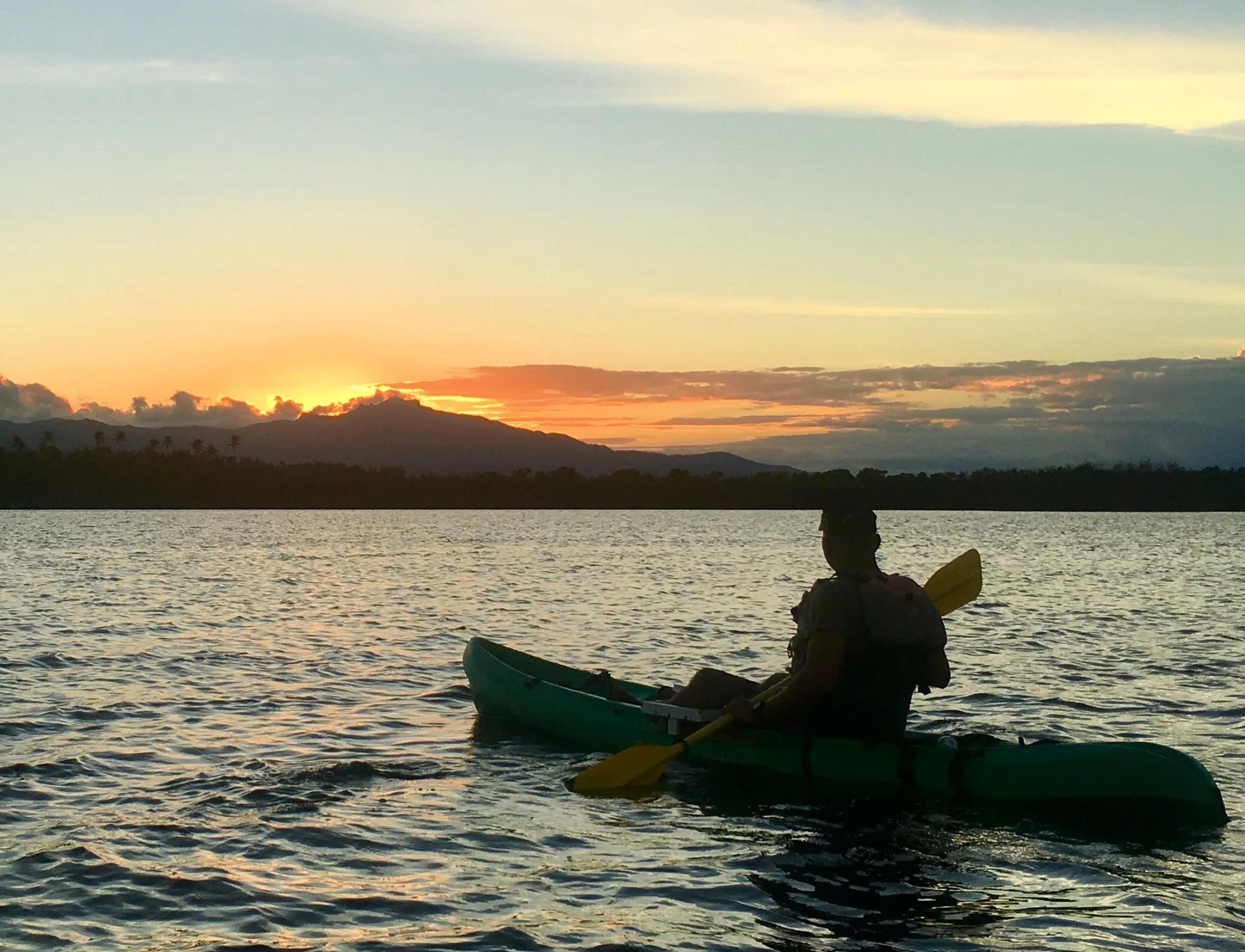 Person kayaking at sunset with mountains in the background