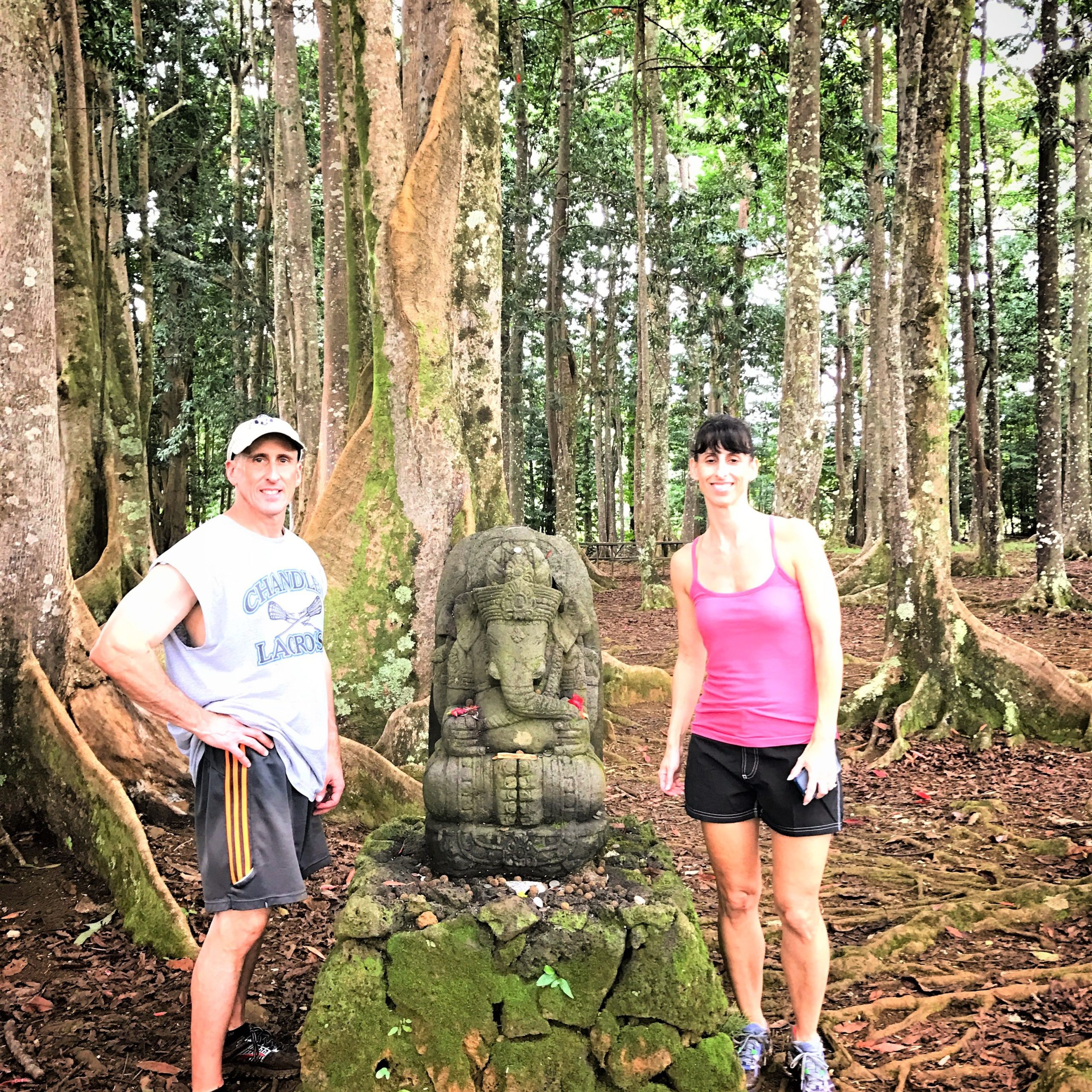 Two people beside a stone statue of Ganesh in a forested area