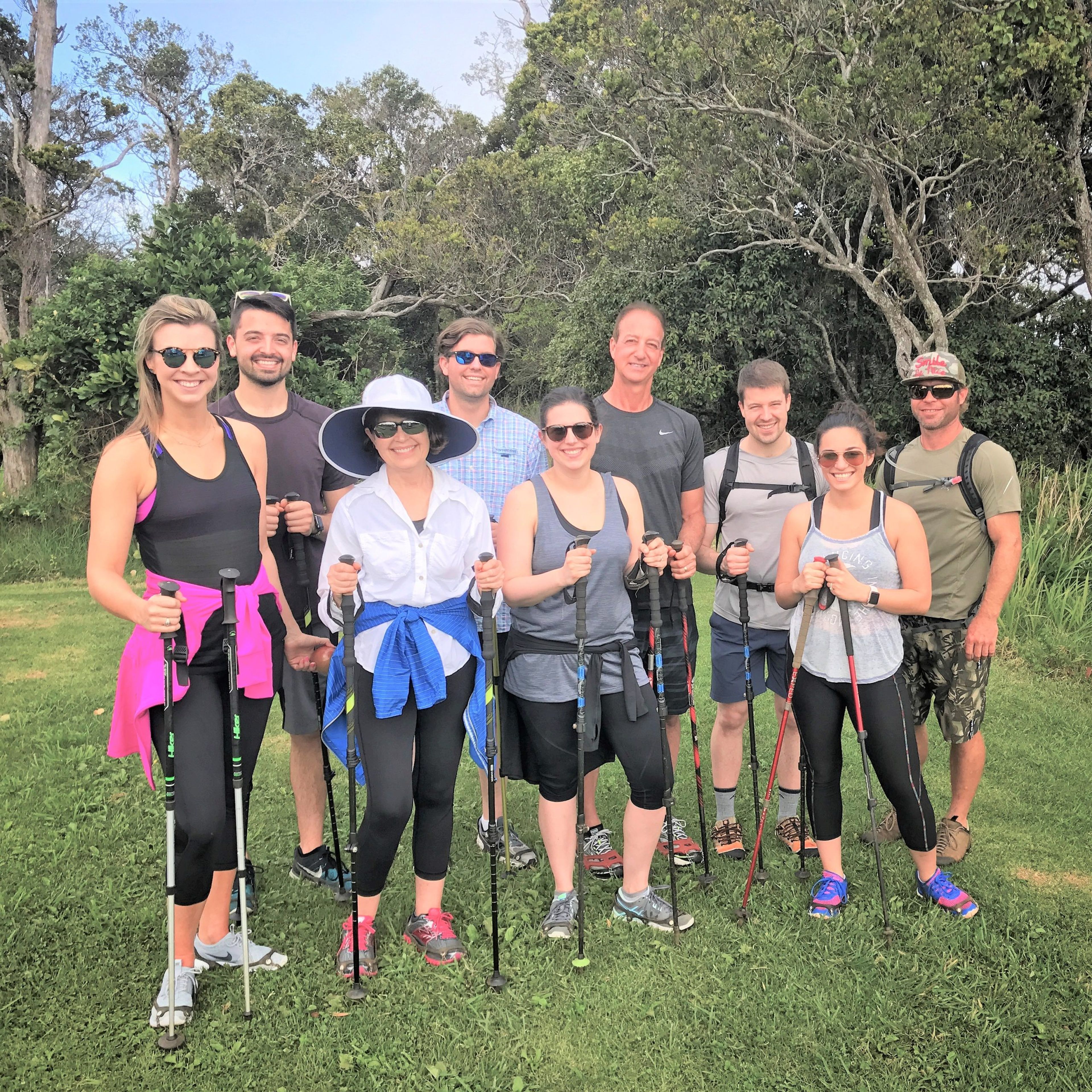 Group of hikers posing outdoors with trekking poles in a lush green setting