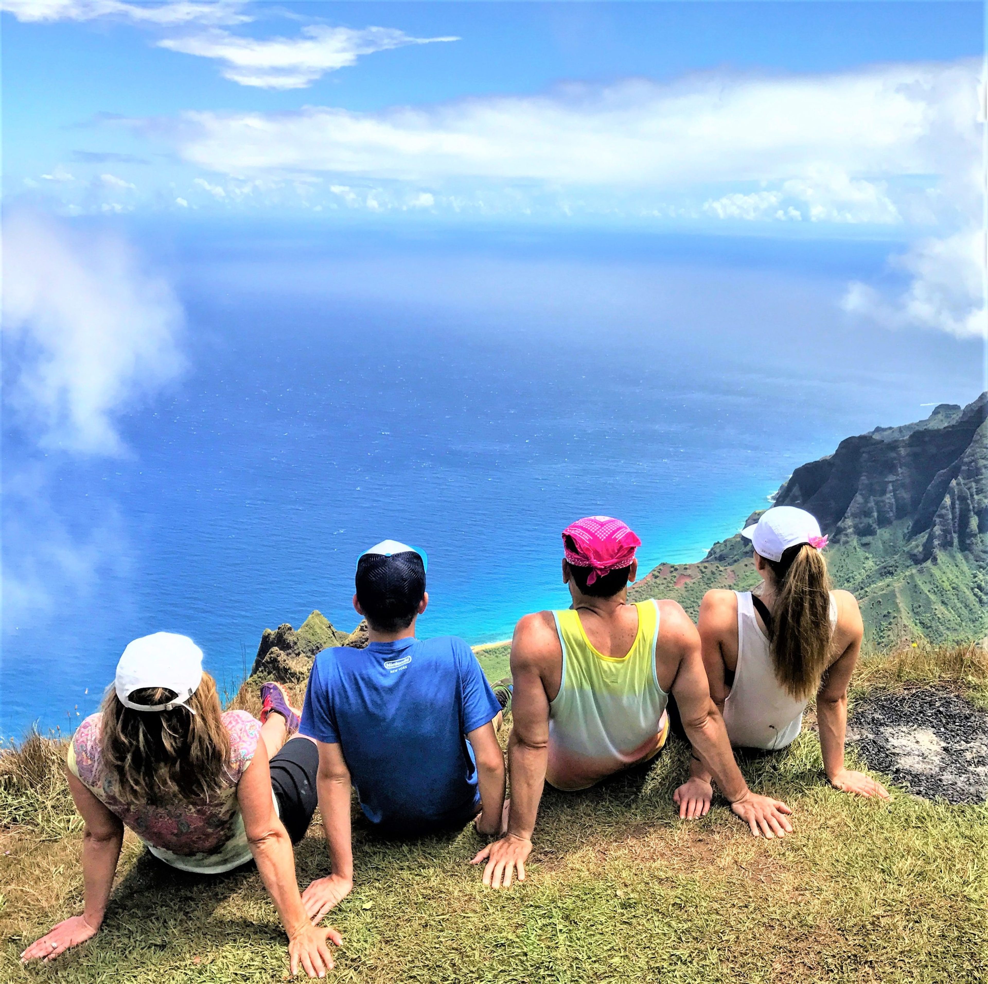 Four people sitting on a cliff overlooking the ocean and mountains.