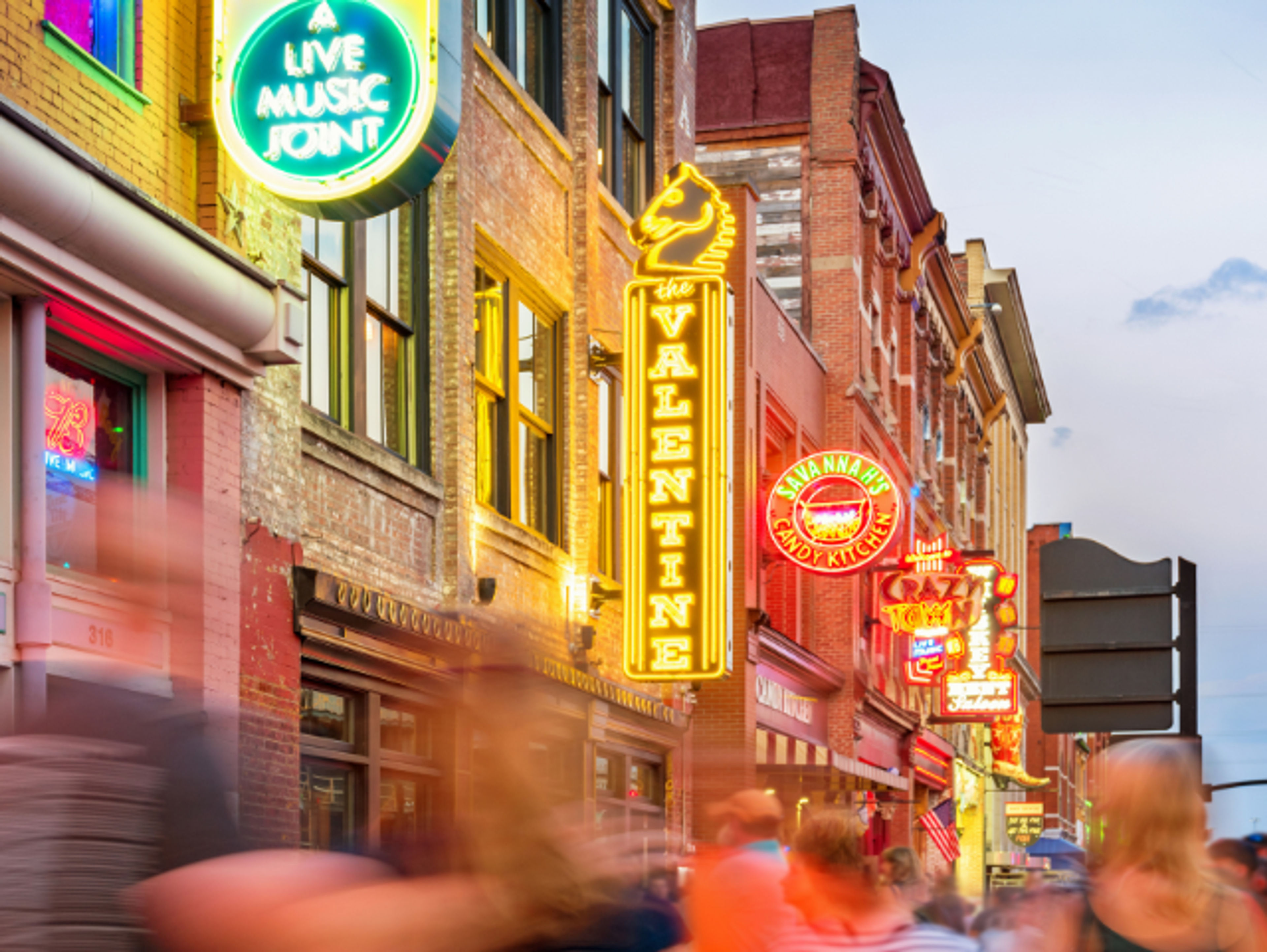 Colorful neon signs on a lively street with blurred pedestrians.