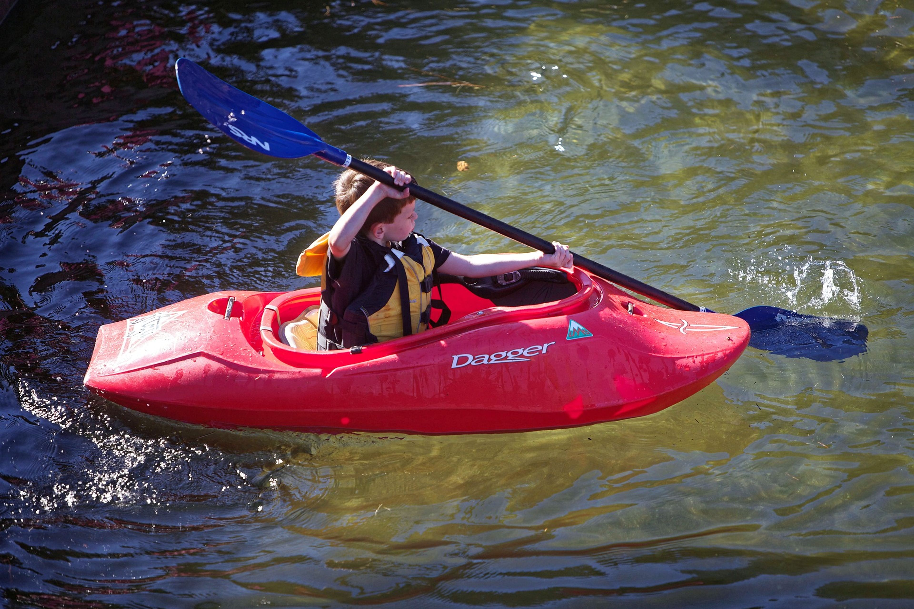 A child kayaking in a red kayak on calm water with a paddle.