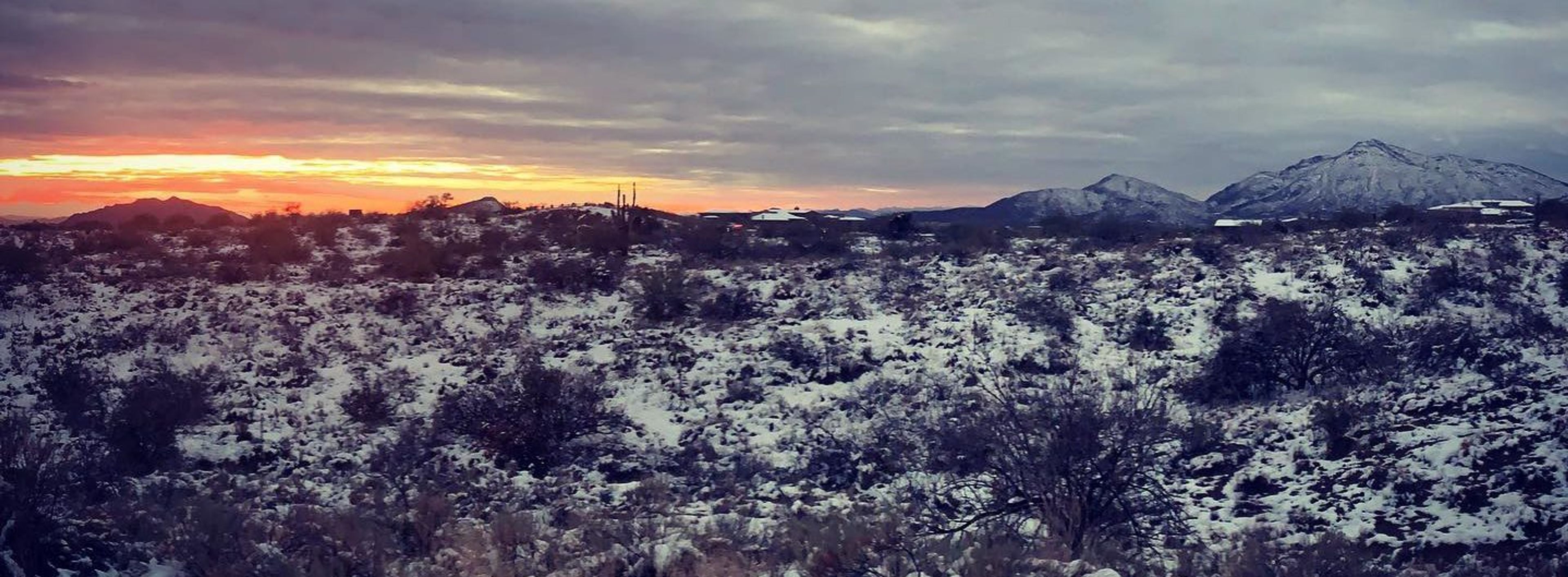 Snow-covered landscape with mountains and a colorful sunset in the background