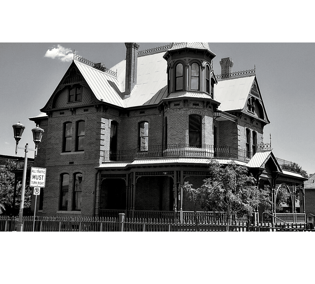 Victorian-style brick mansion with ornate details and a surrounding fence.