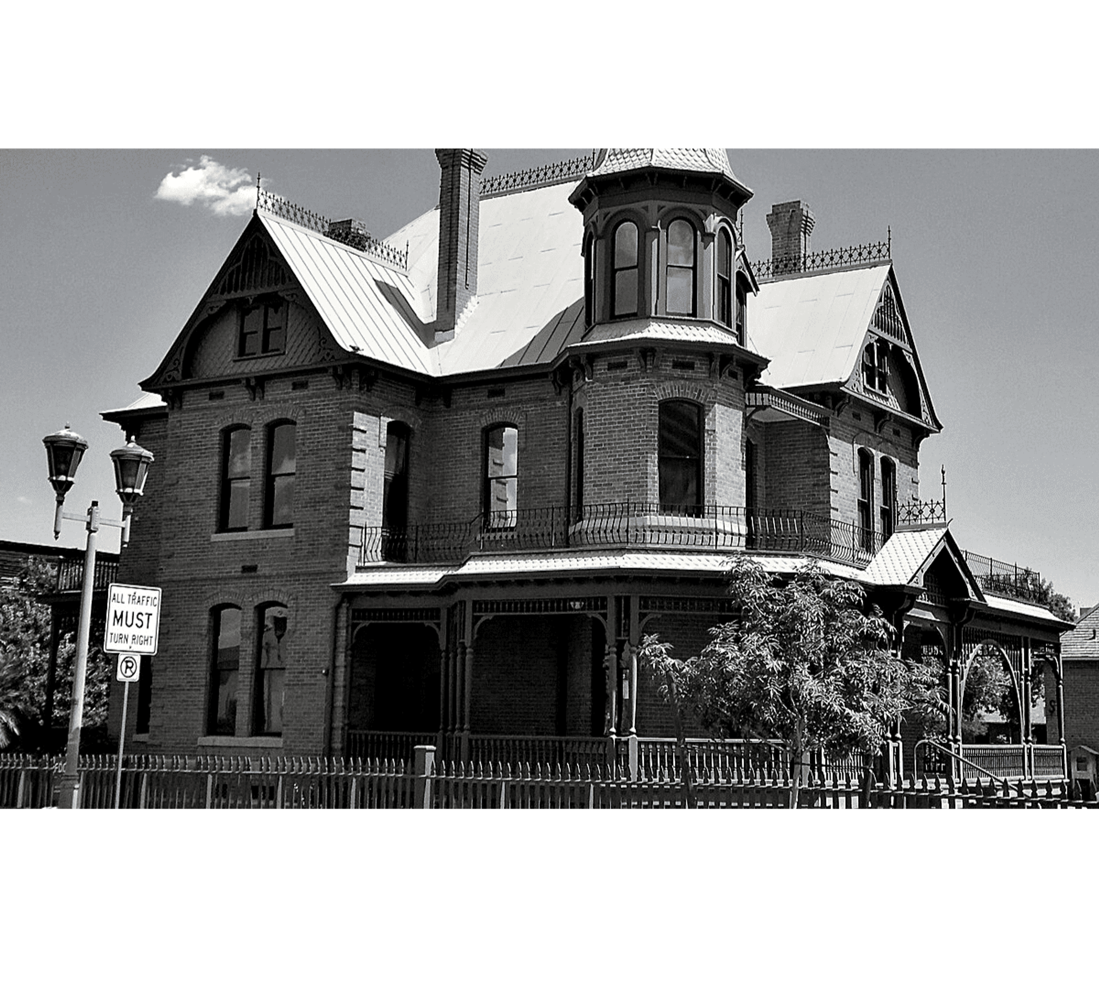 Victorian-style brick mansion with ornate details and a surrounding fence.