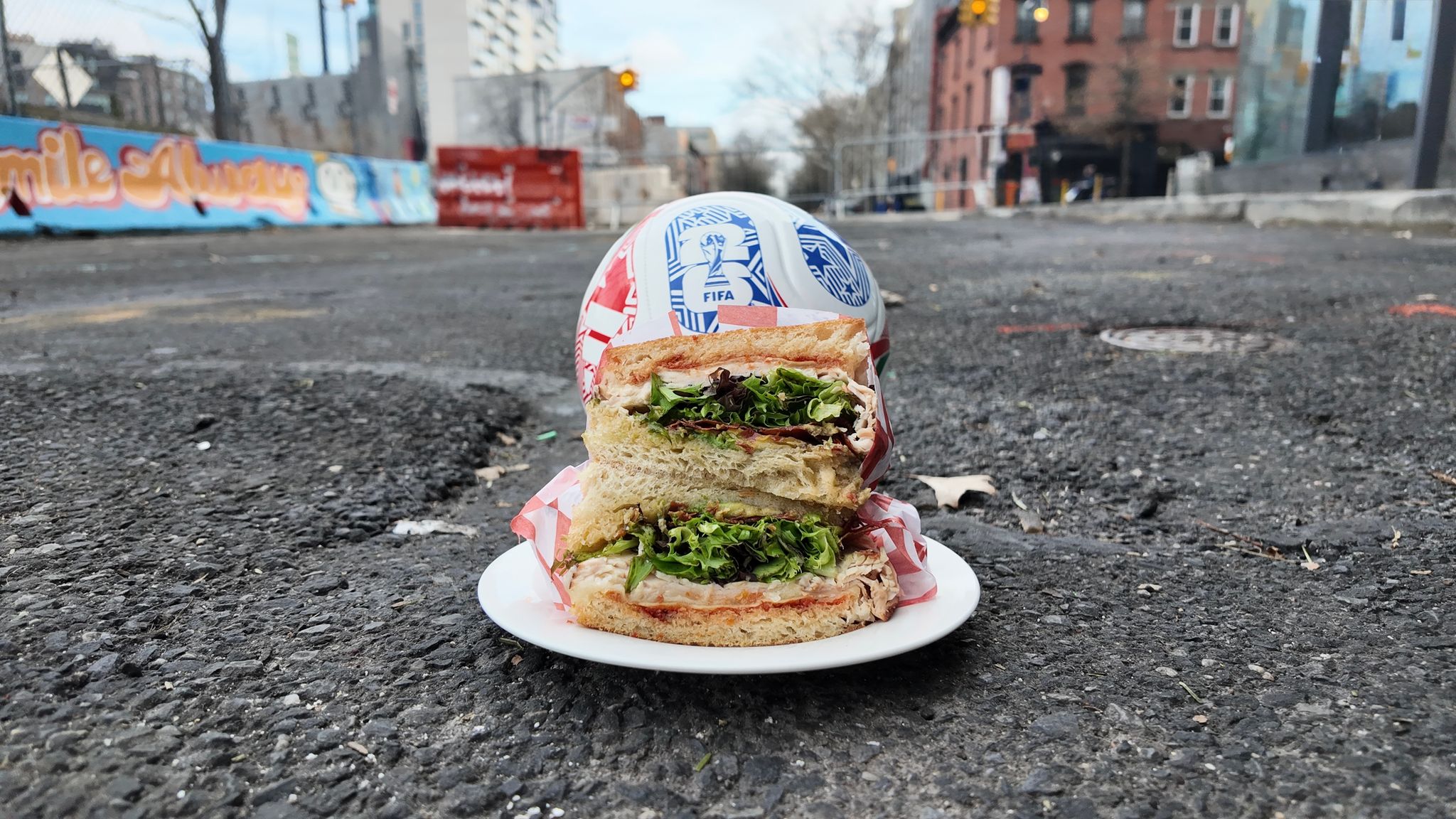 A sandwich on a plate with a soccer ball in the background on a street.