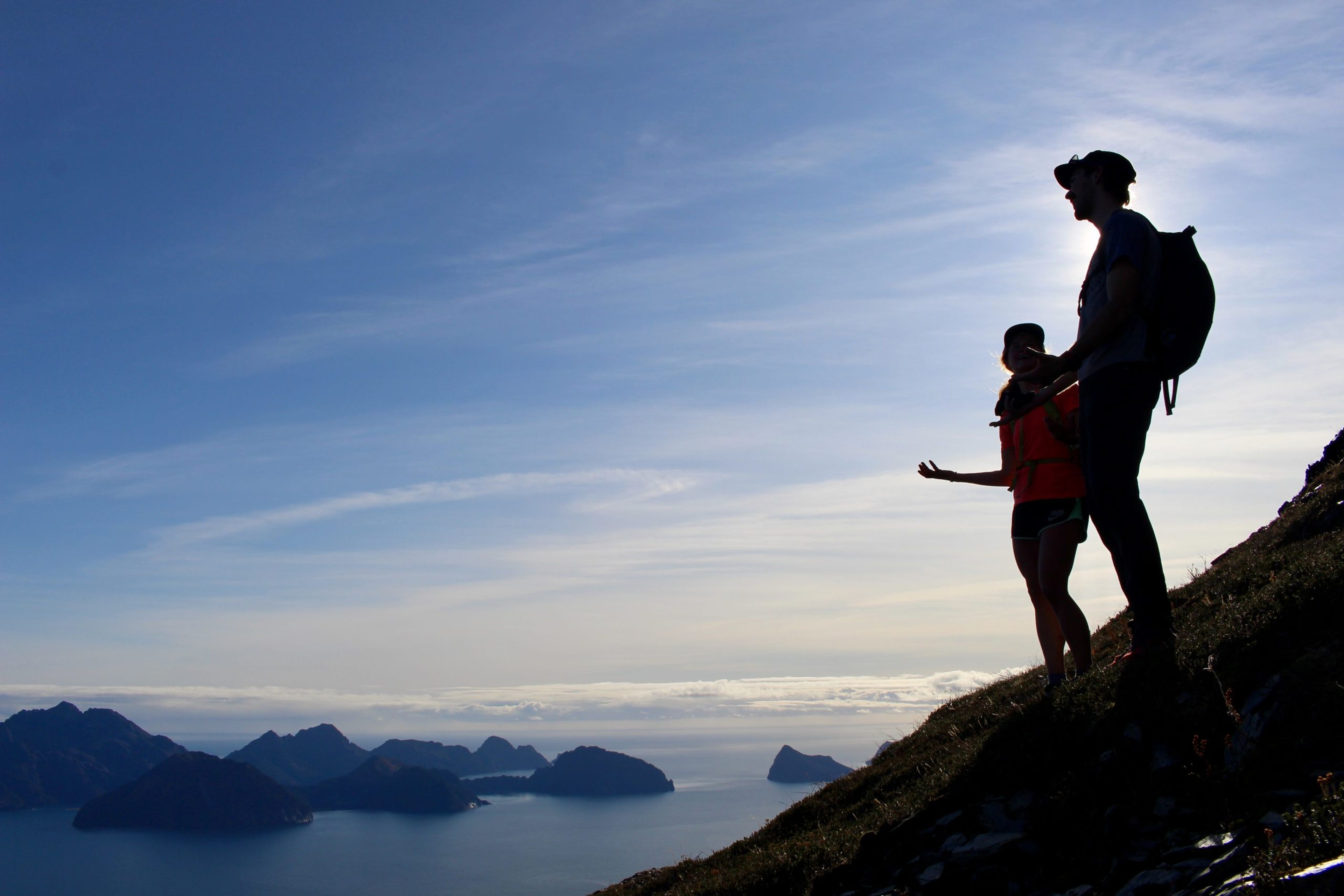 Two hikers silhouetted against a scenic mountain and ocean backdrop.