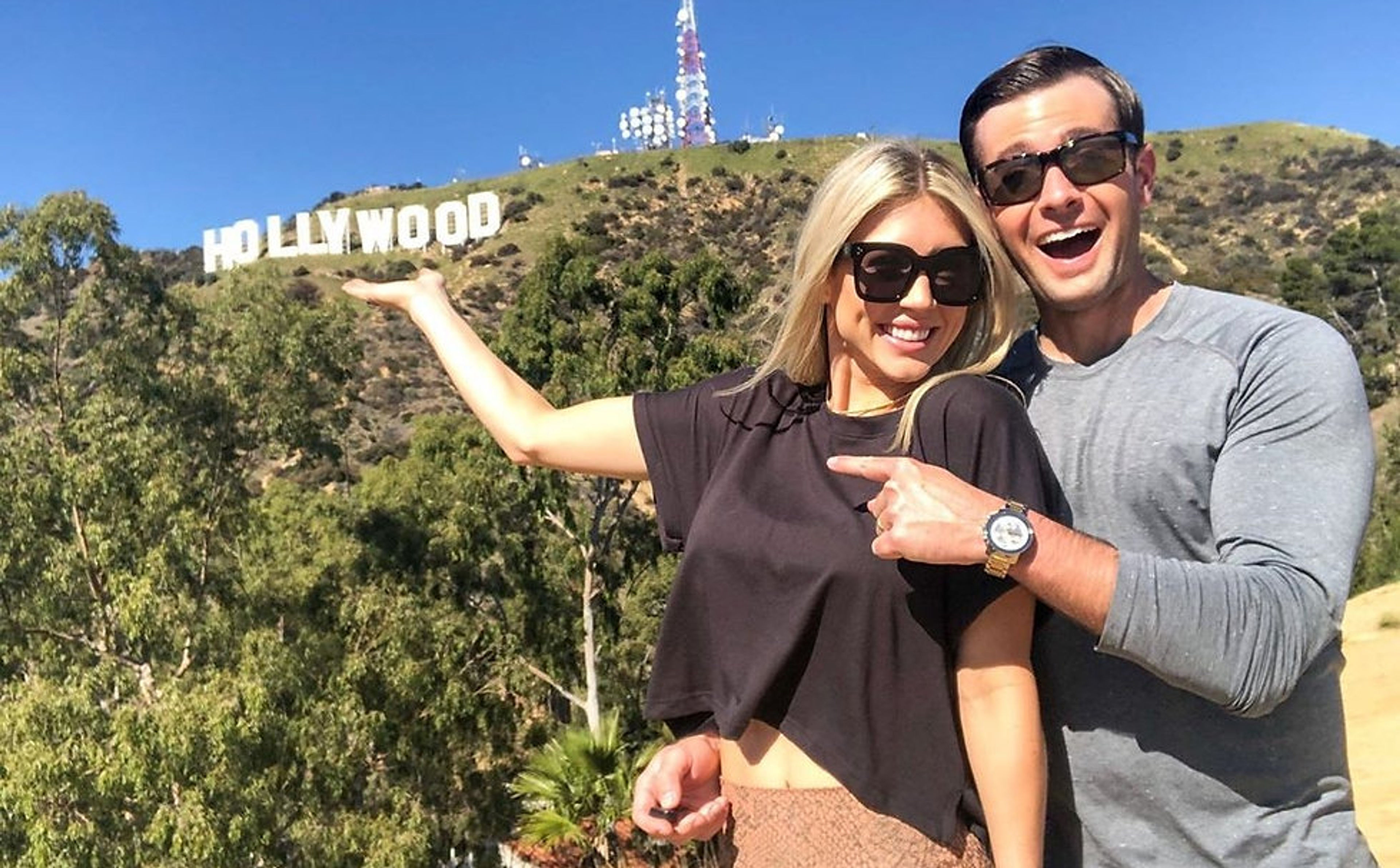 Two people posing with the Hollywood sign in the background on a sunny day.
