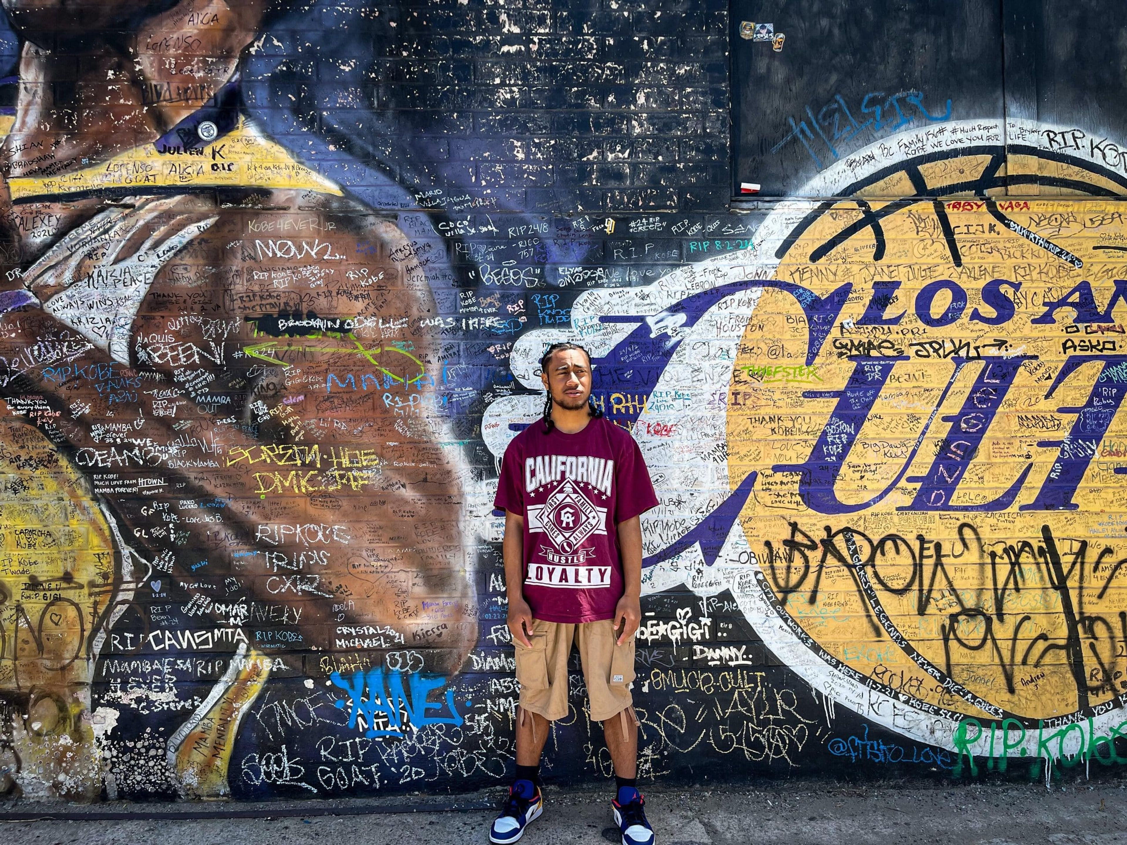 Person standing in front of a mural with graffiti and tribute messages.