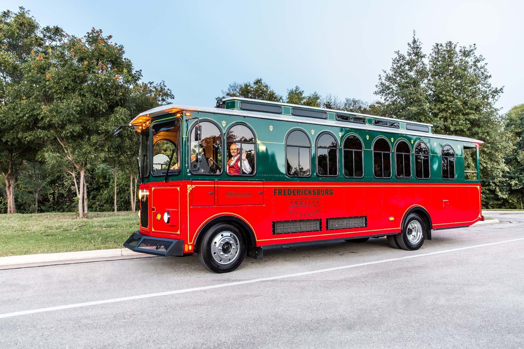 A red and green trolley bus parked with trees in the background.