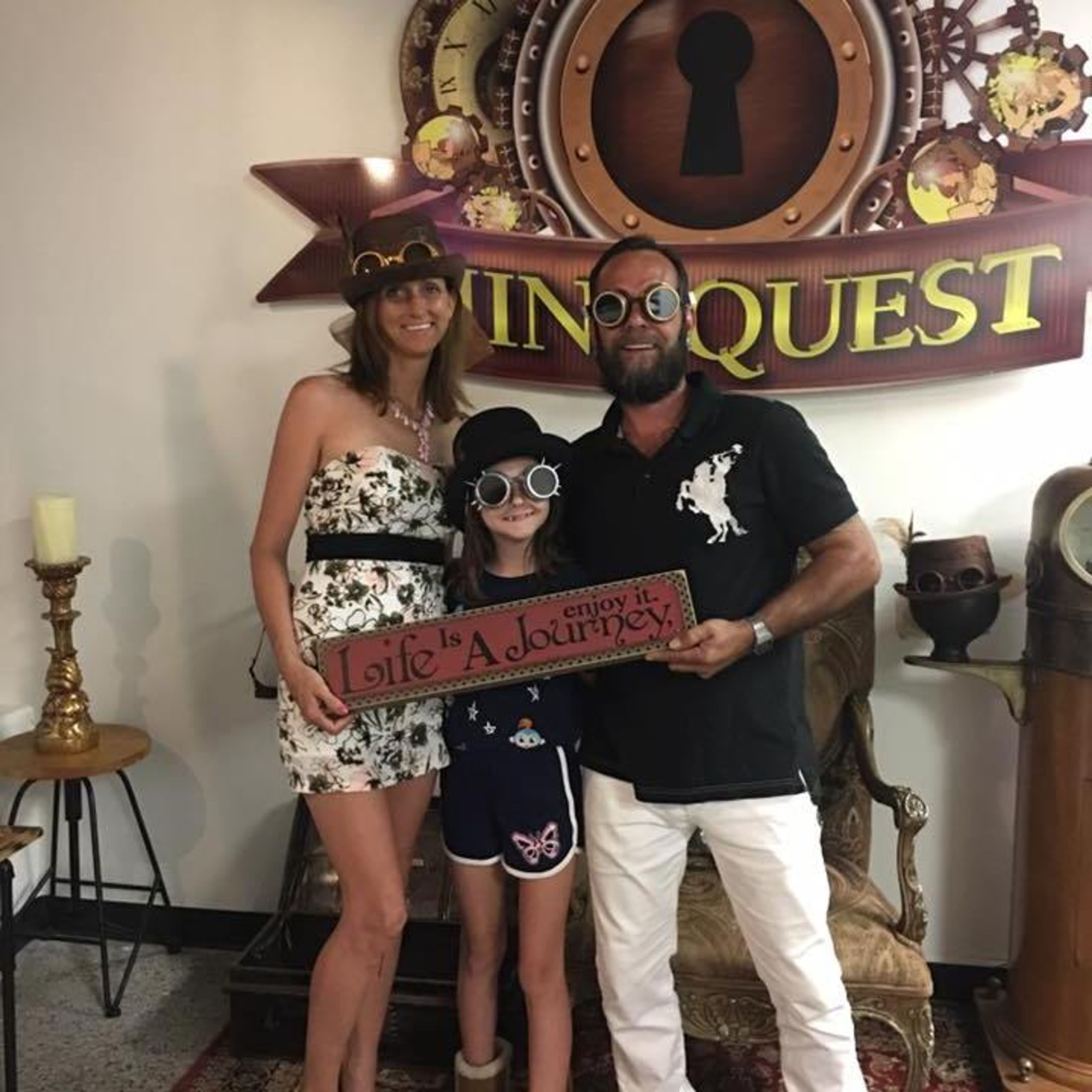 Three people posing together in a themed room with a sign that says 'Life Is A Journey.'