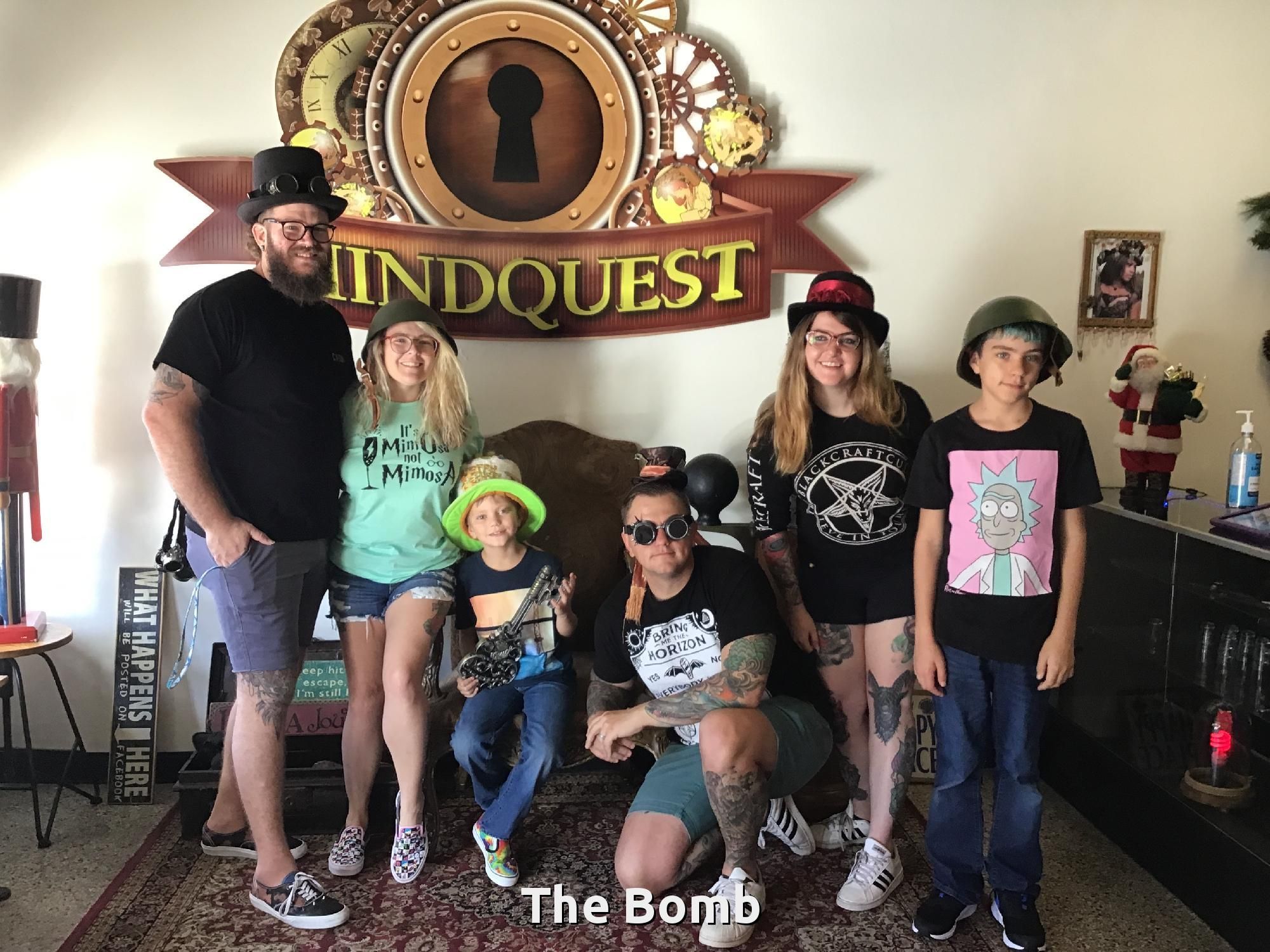 Group of people posing in front of a Mindquest sign, some wearing hats and holding props.