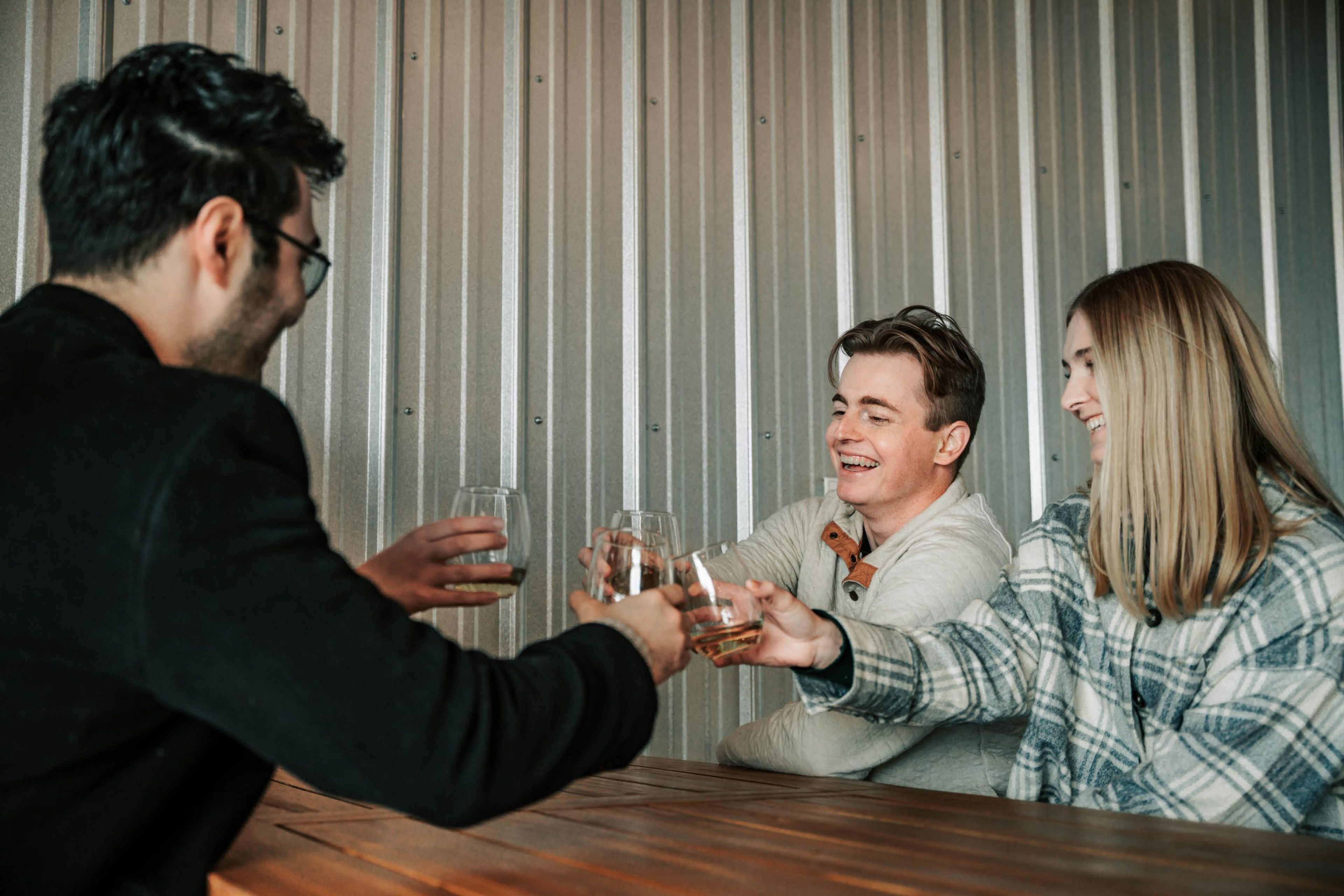 Three friends toasting with drinks at a wooden table in a casual setting.