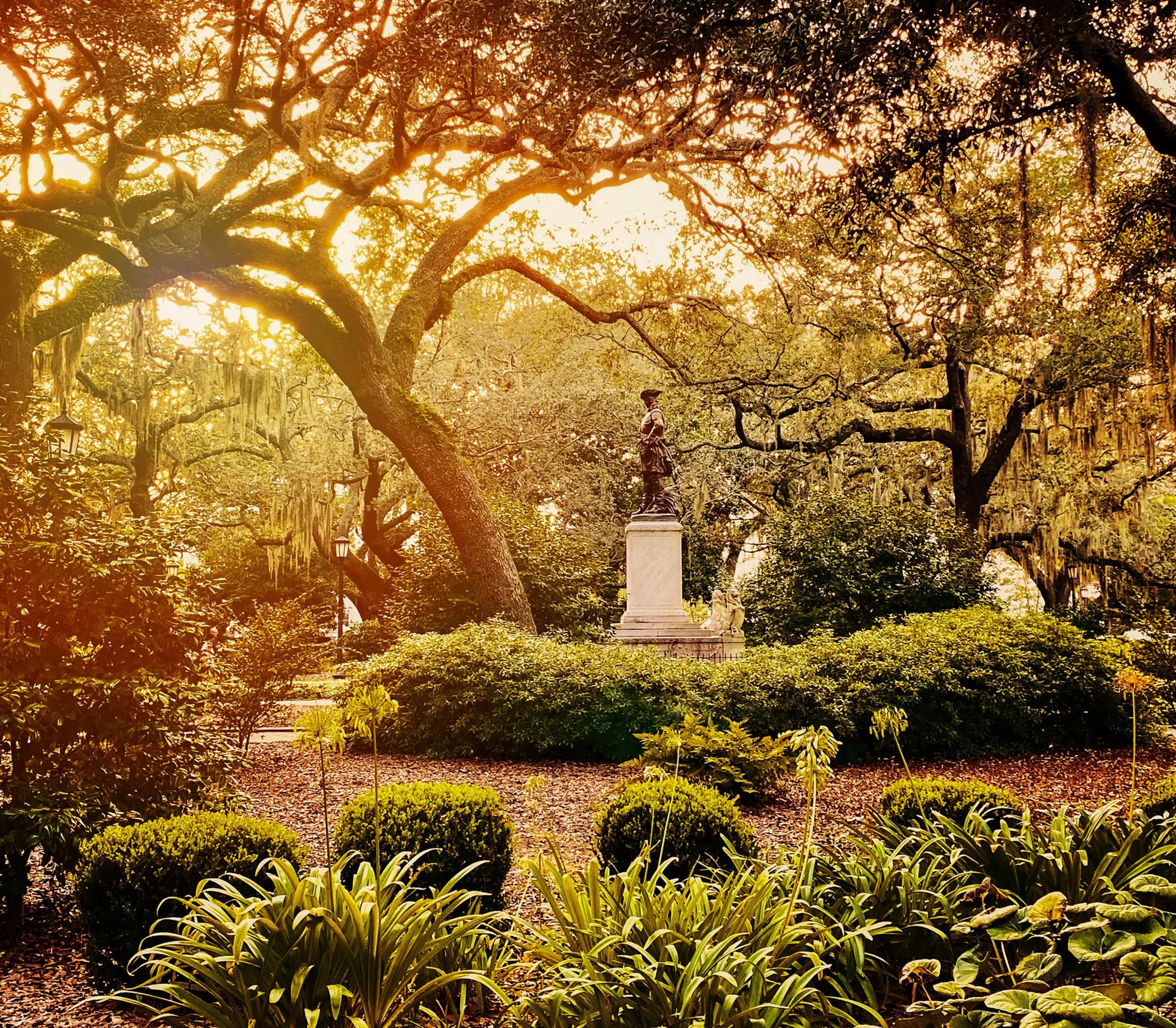 Statue in a lush park with trees and greenery at sunset