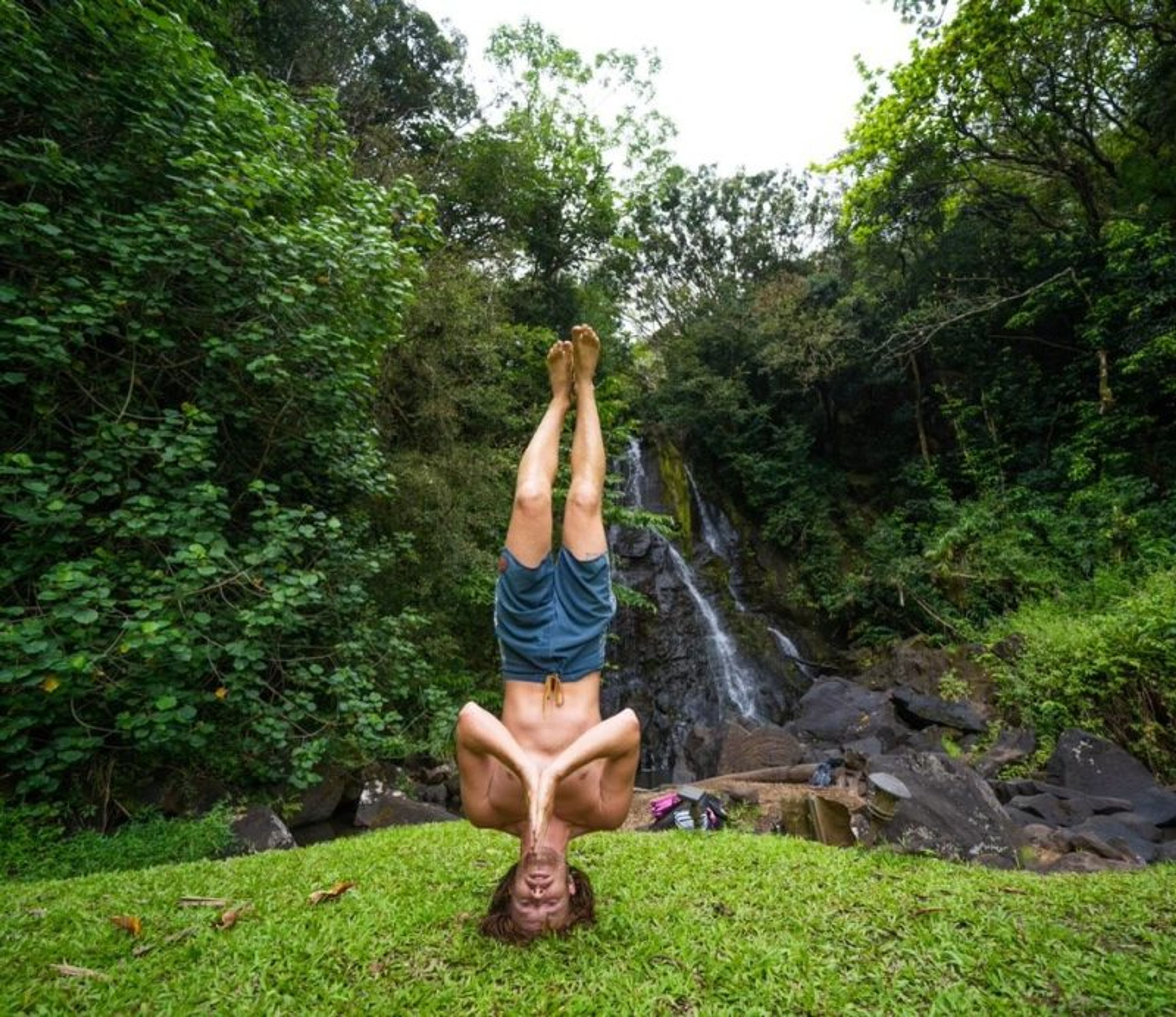 Person performing a handstand in front of a waterfall surrounded by greenery.