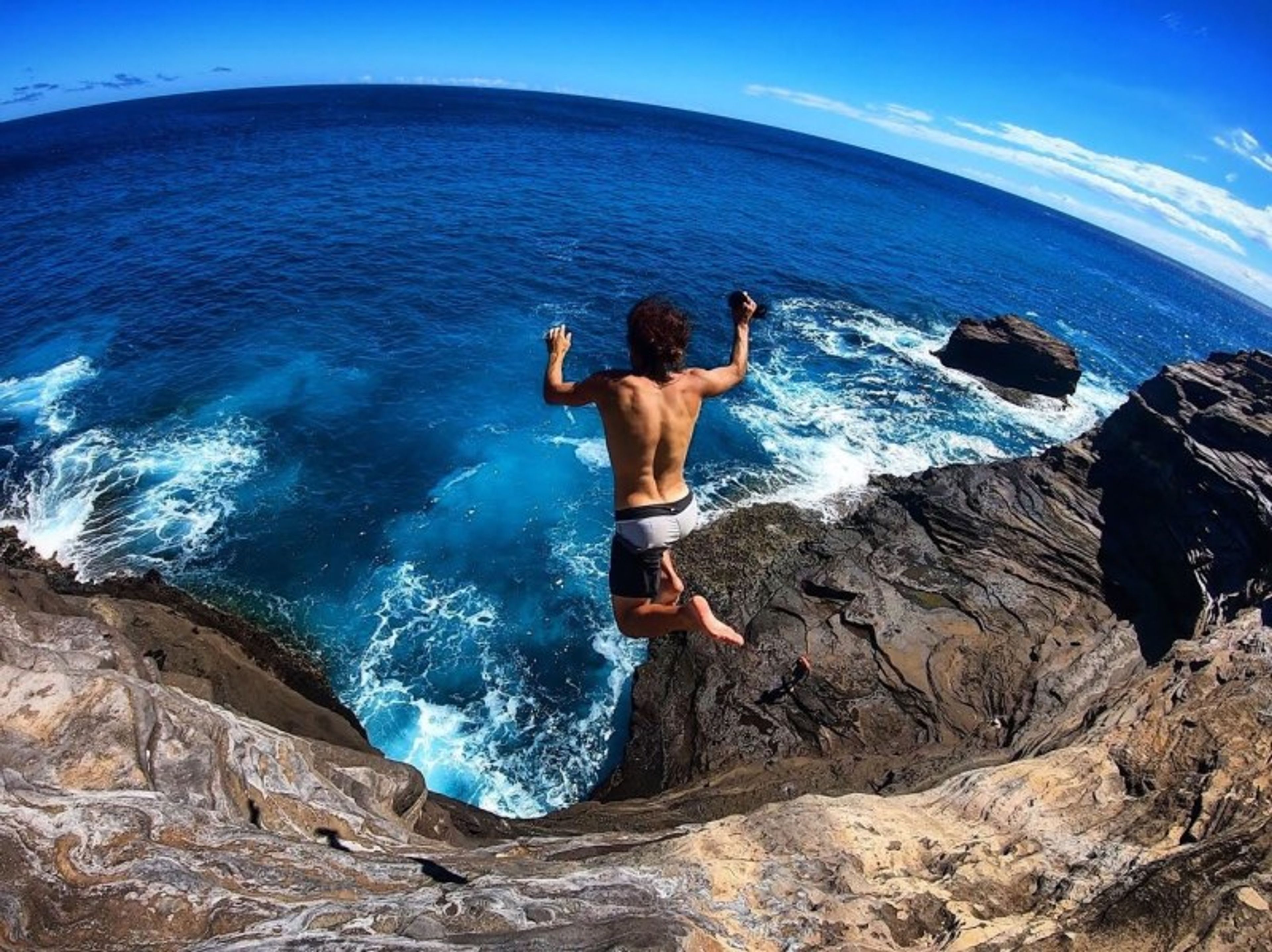 Person jumping off a rocky cliff into the ocean