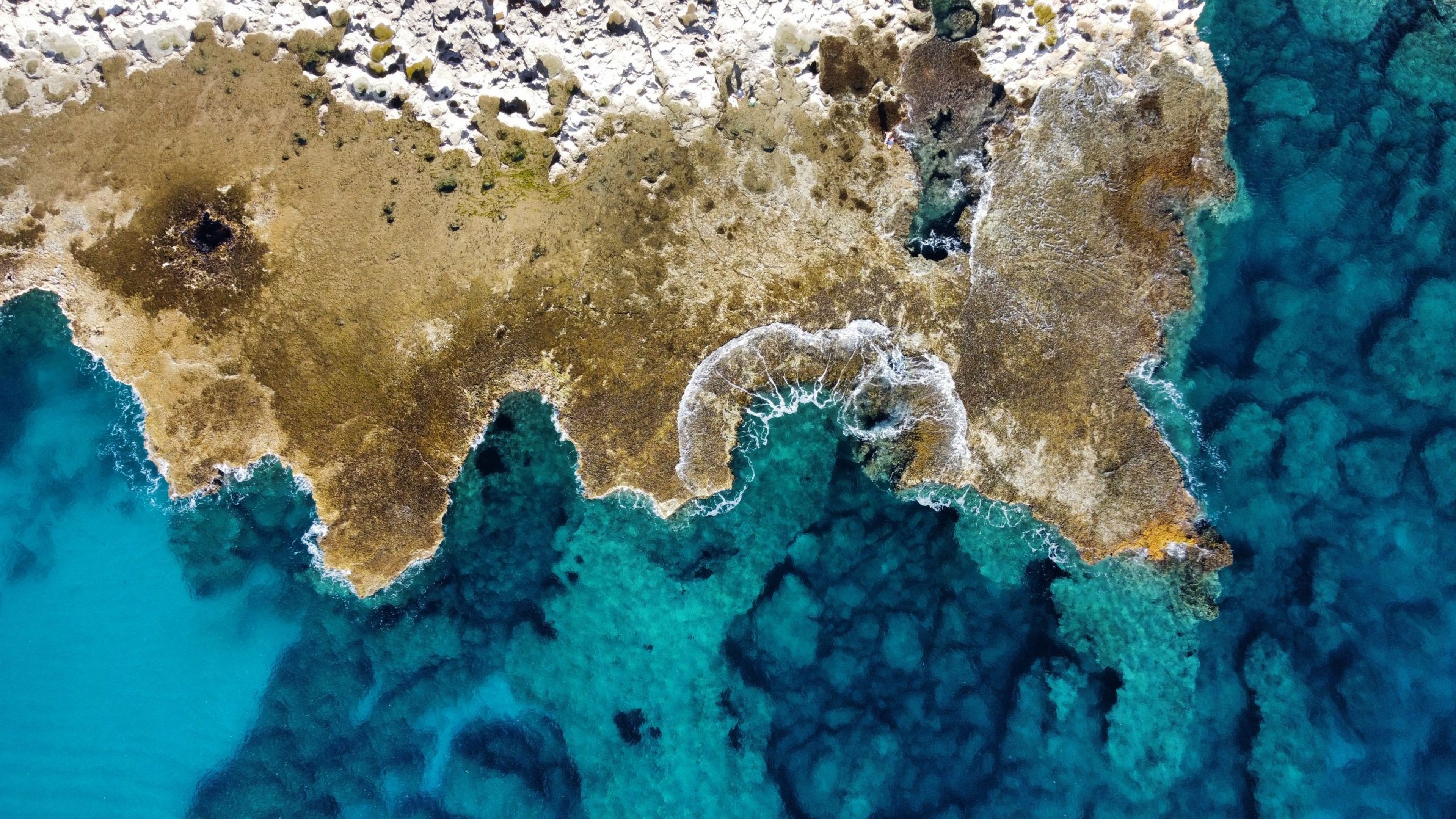 Aerial view of rocky coastline meeting clear blue water.