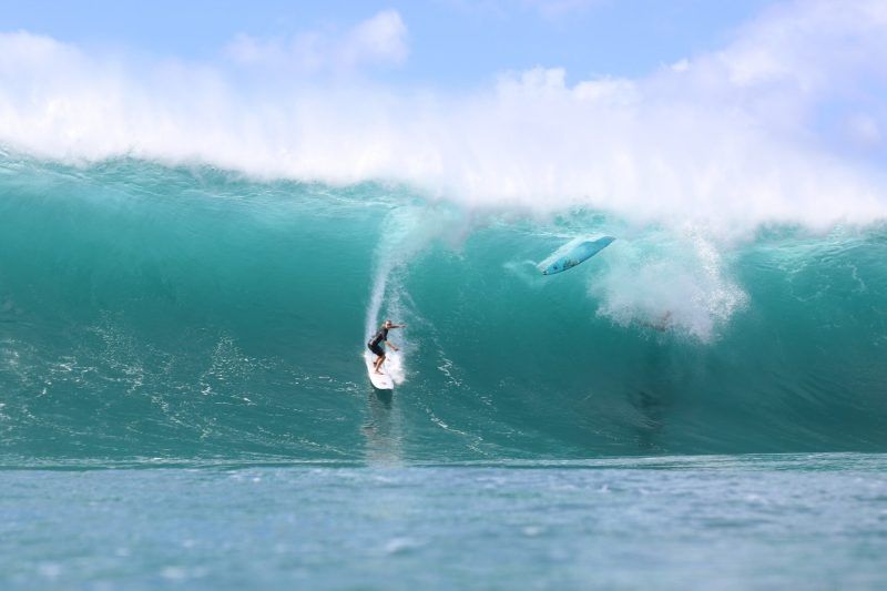 Surfer riding a large wave with another surfboard in the air.