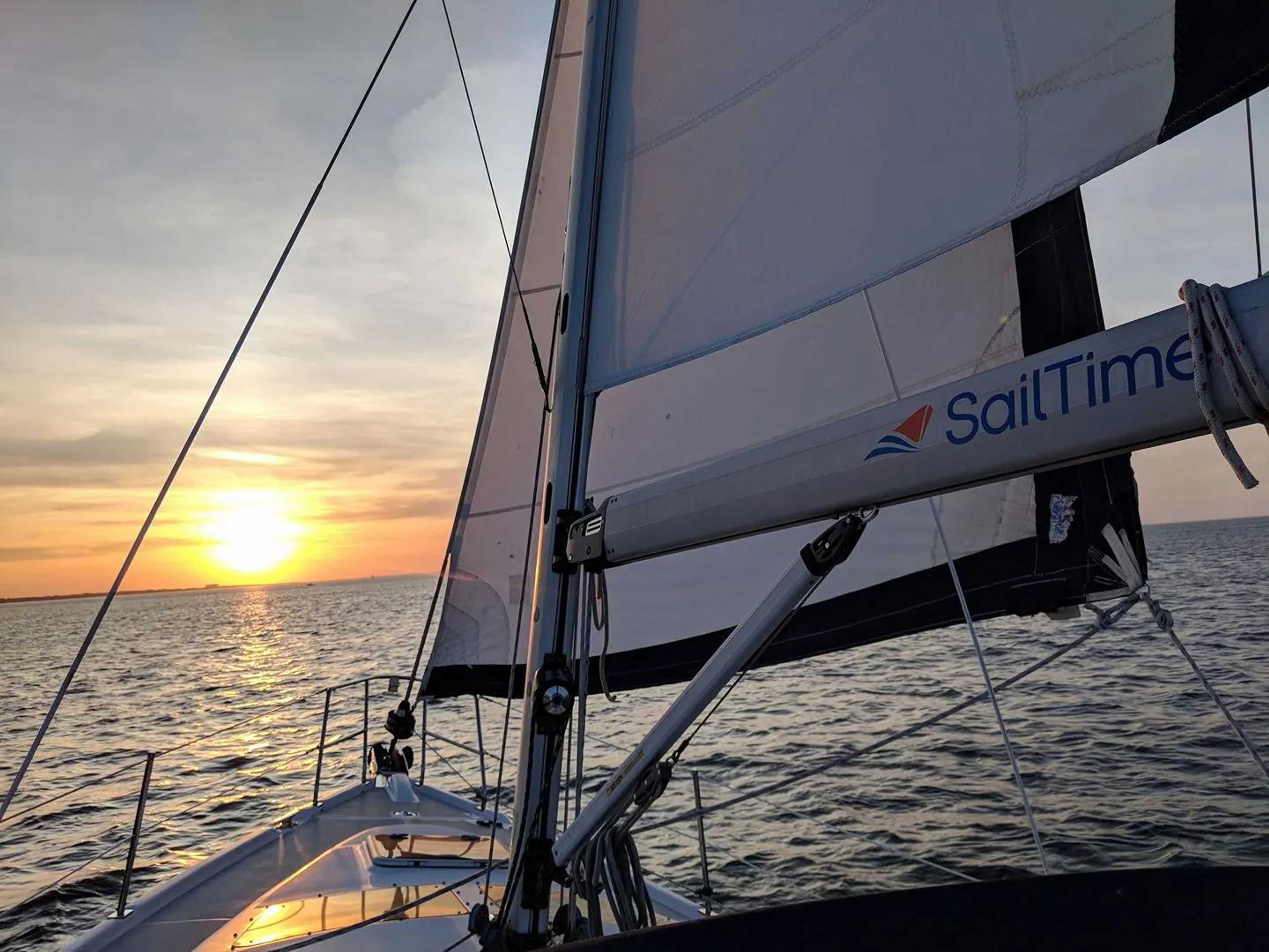 Sailboat with sails up on water during sunset