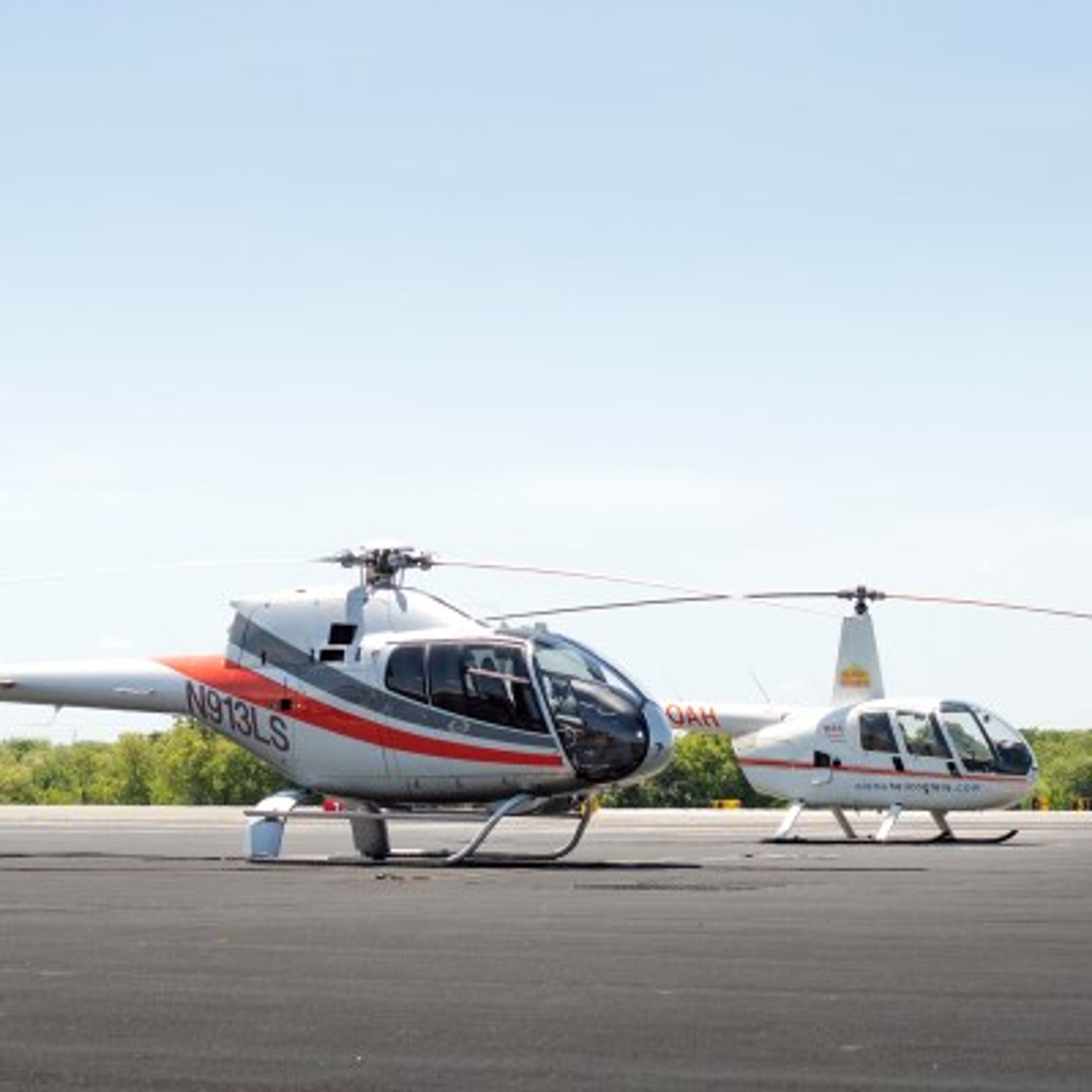 Two helicopters parked on a tarmac under a clear blue sky.