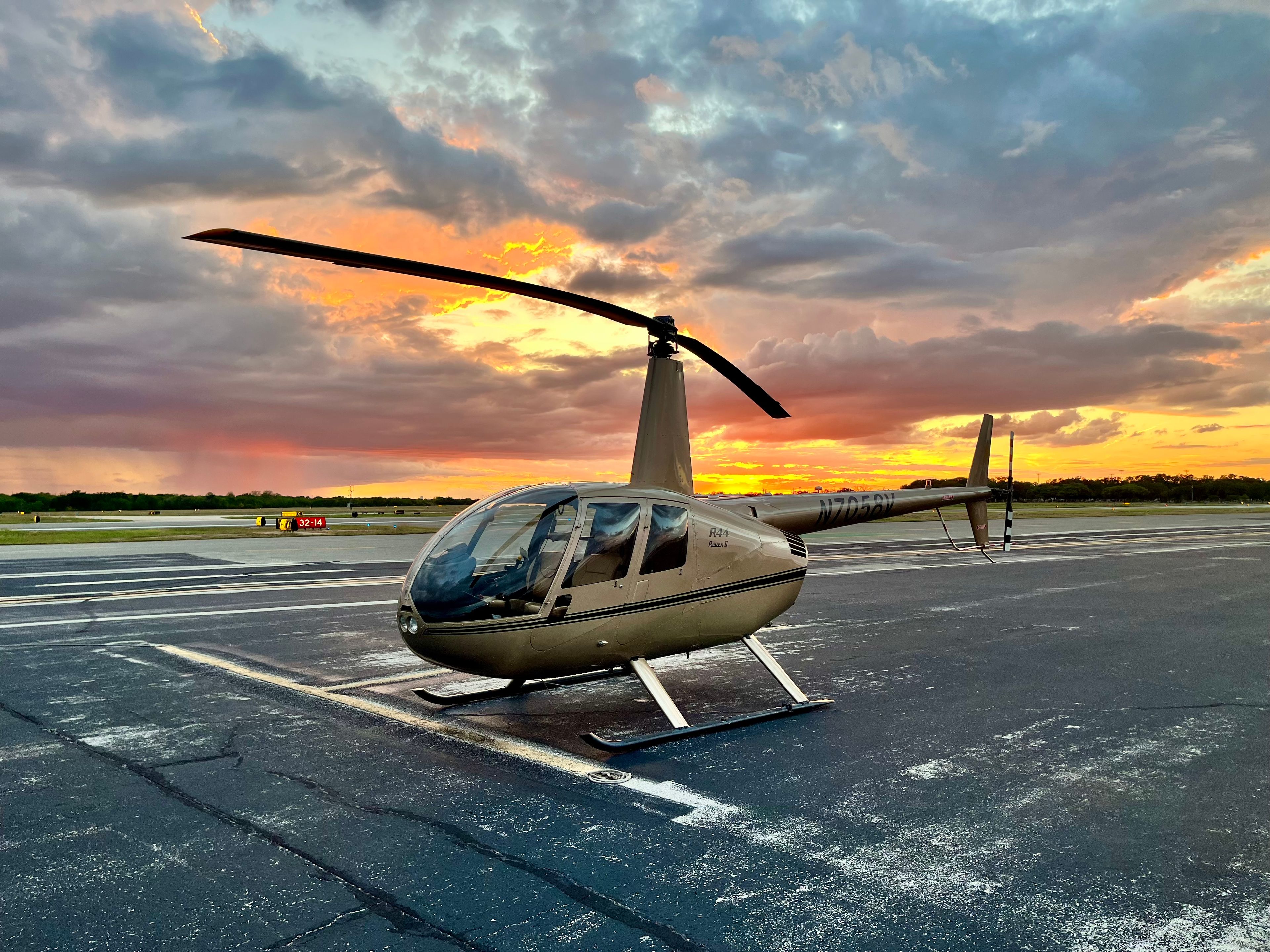 A helicopter parked on a runway during a colorful sunset.