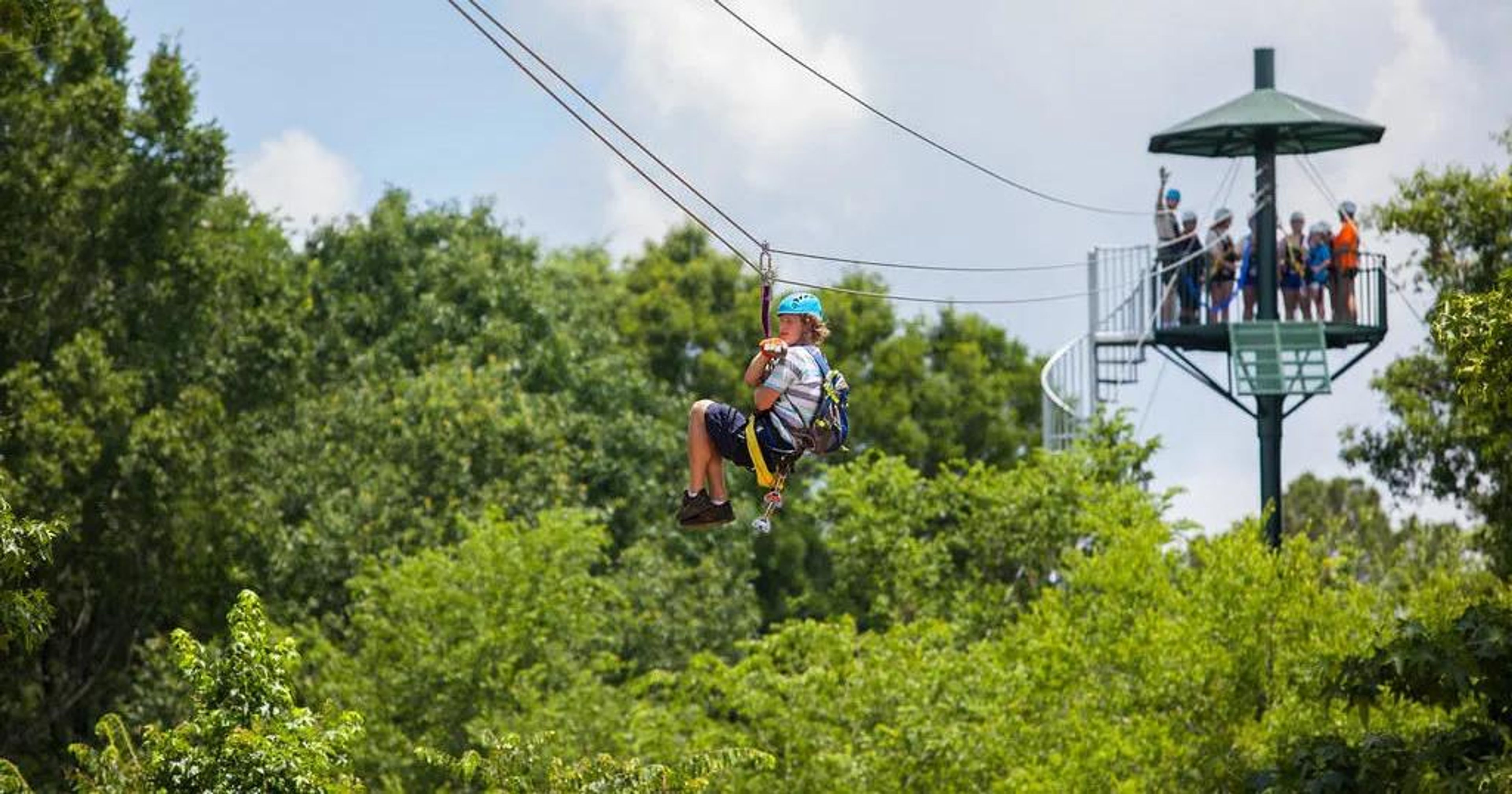 A child zip-lining through trees with a viewing platform in the background.