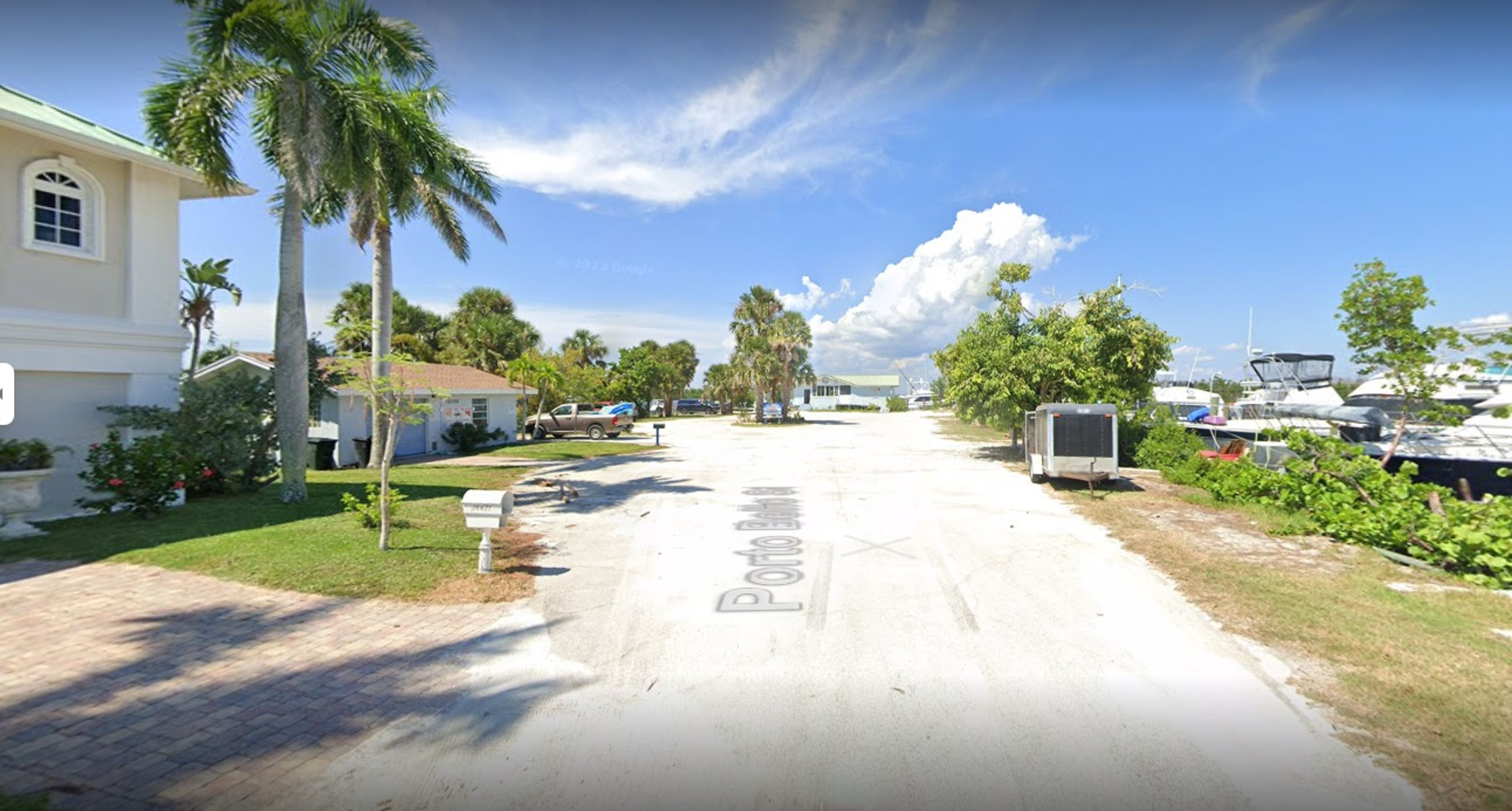 A quiet street lined with palm trees and boats in a marina.