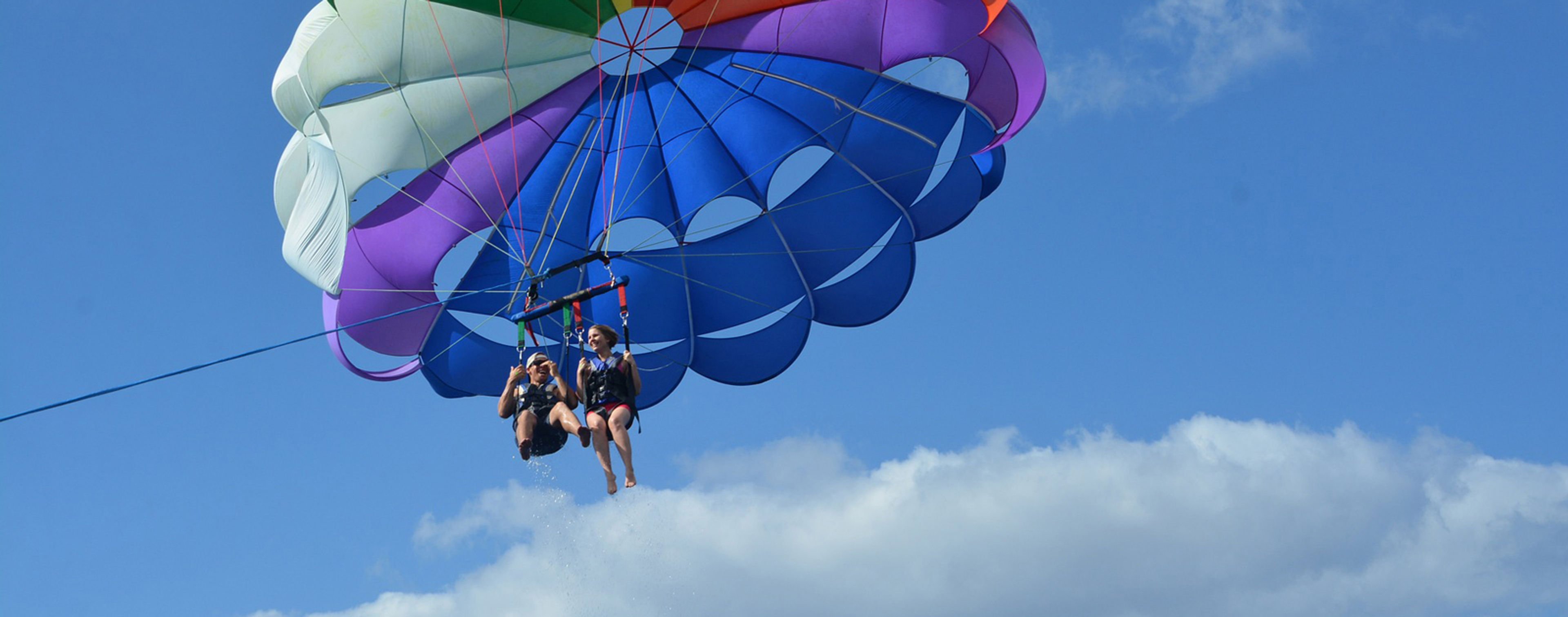 Two people parasailing under a colorful parachute against a blue sky.