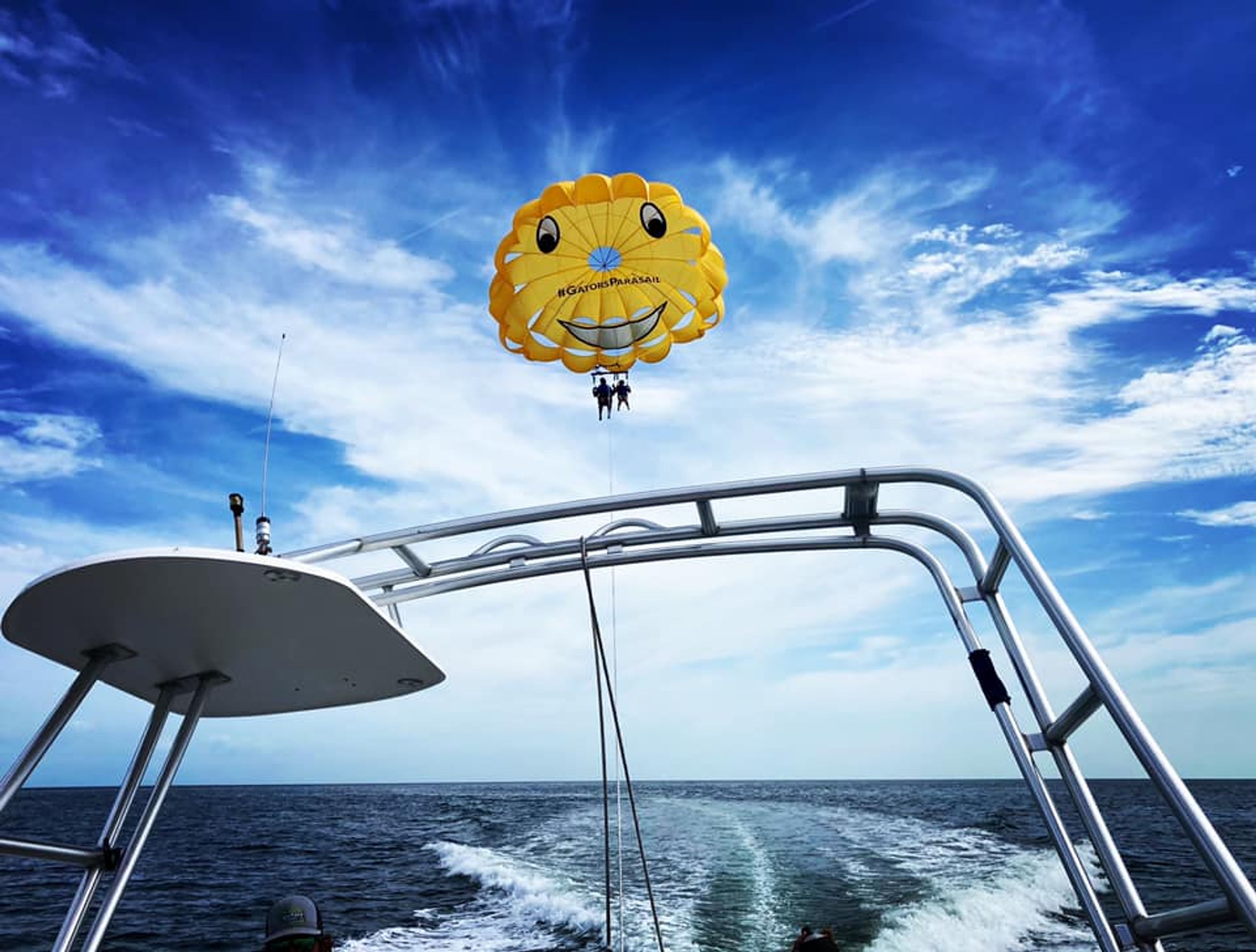 Two people parasailing with a yellow smiley face parachute over the ocean.