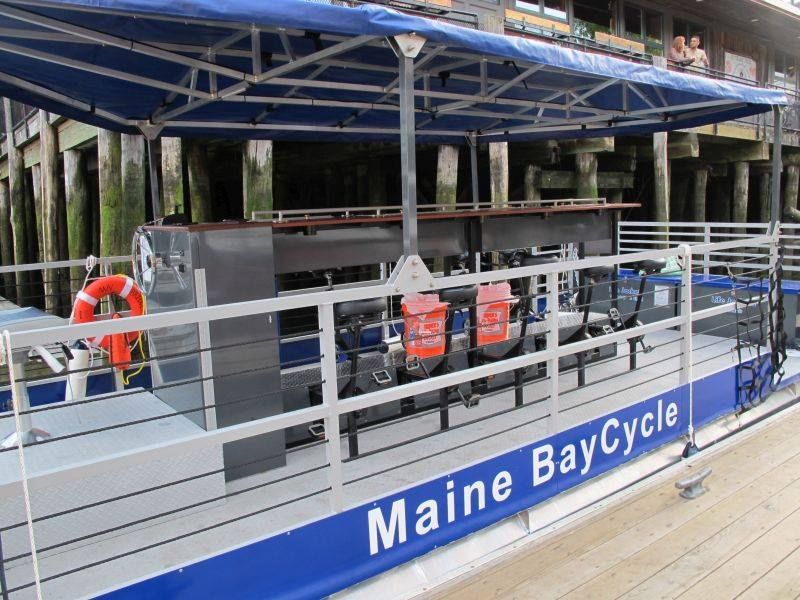 A boat named Maine BayCycle with seating and safety equipment at a dock.